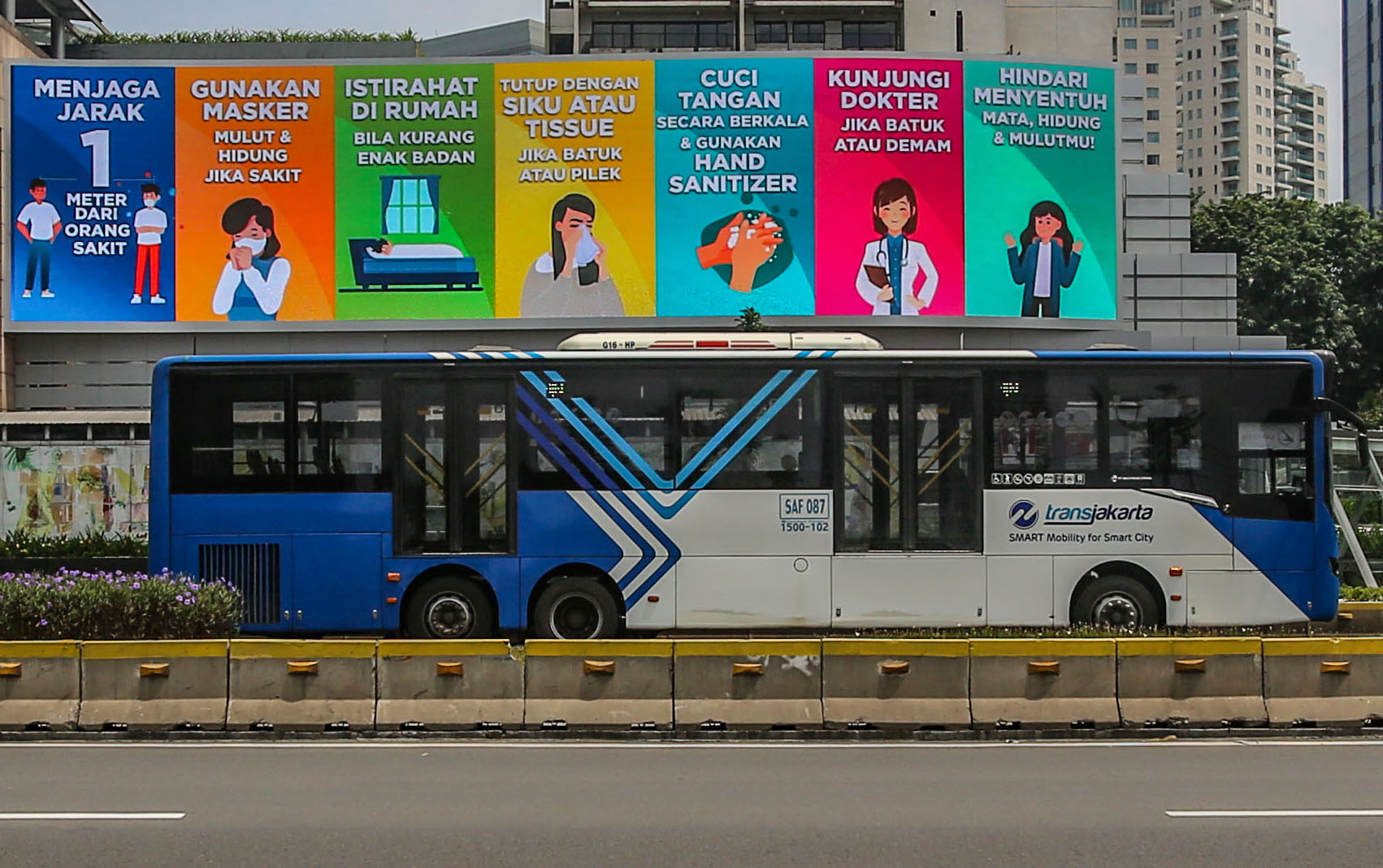 Bus TransJakarta melintas di dekat papan himbauan pencegahan penyebaran virus korona di Jakarta.