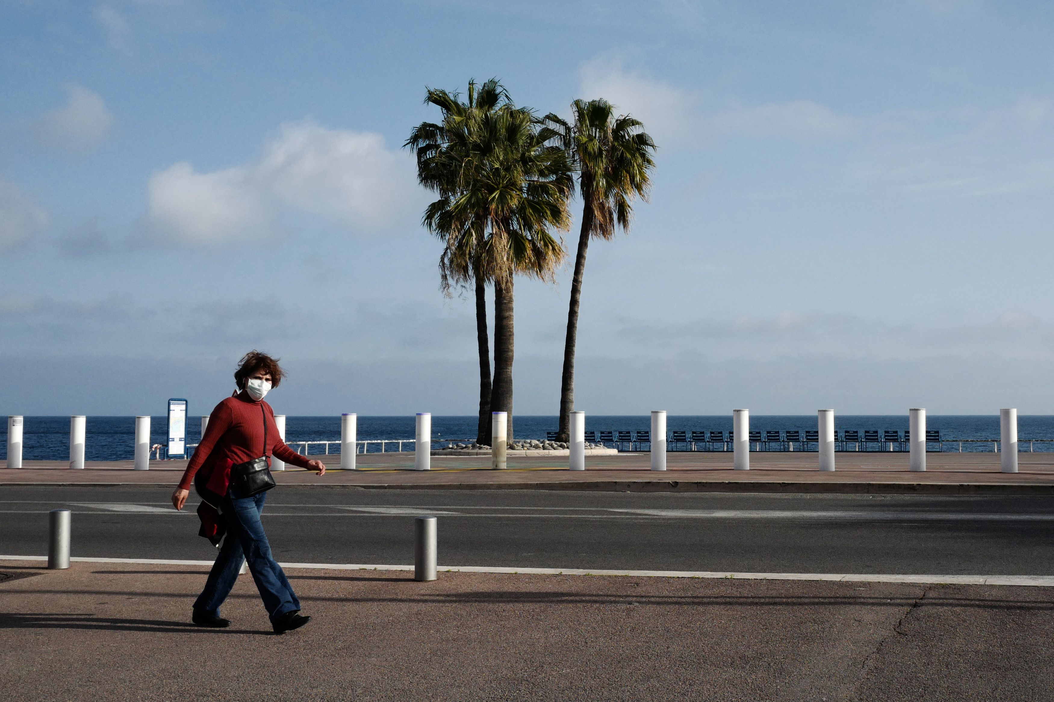 Seorang perempuan mengenakan masker berjalan di tepi pantai di Nice, Prancis.