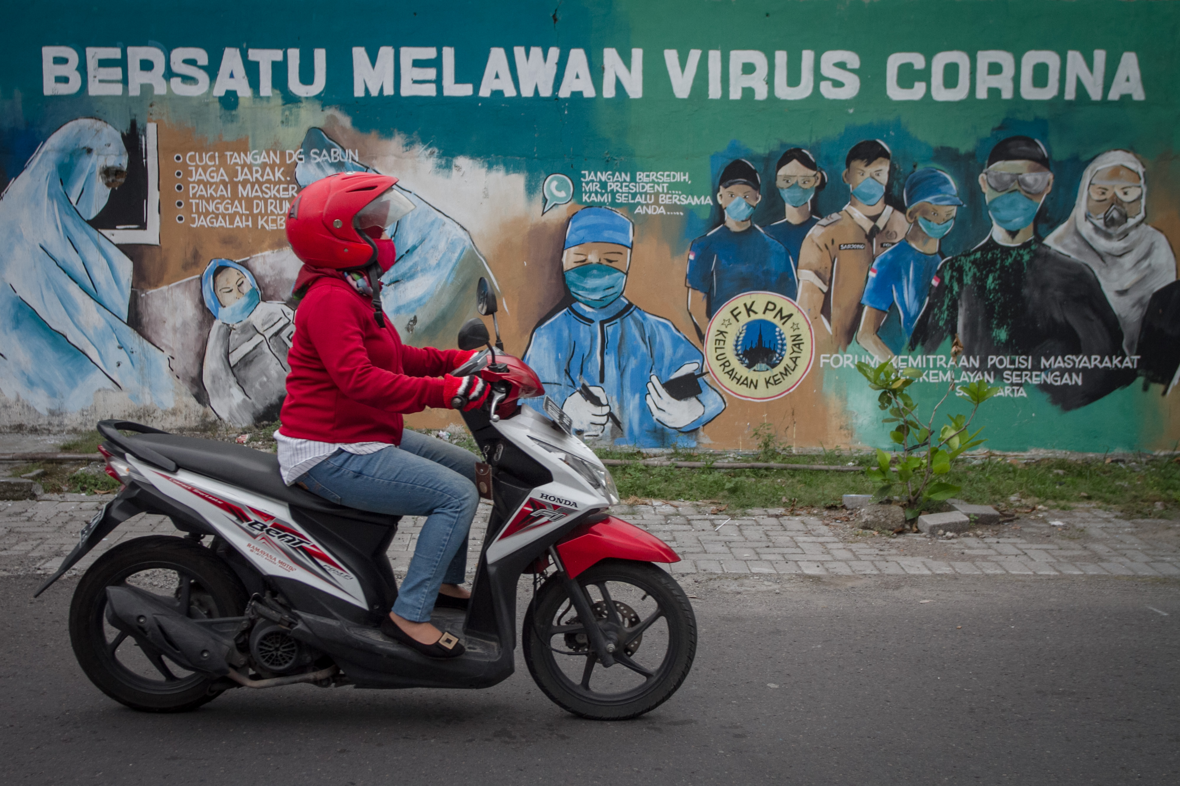 Warga melintas di depan mural bertema Bersatu Melawan COVID-19 di Kampung Kemlayan, Serengan, Solo, Jawa Tengah, Senin (20/4). 