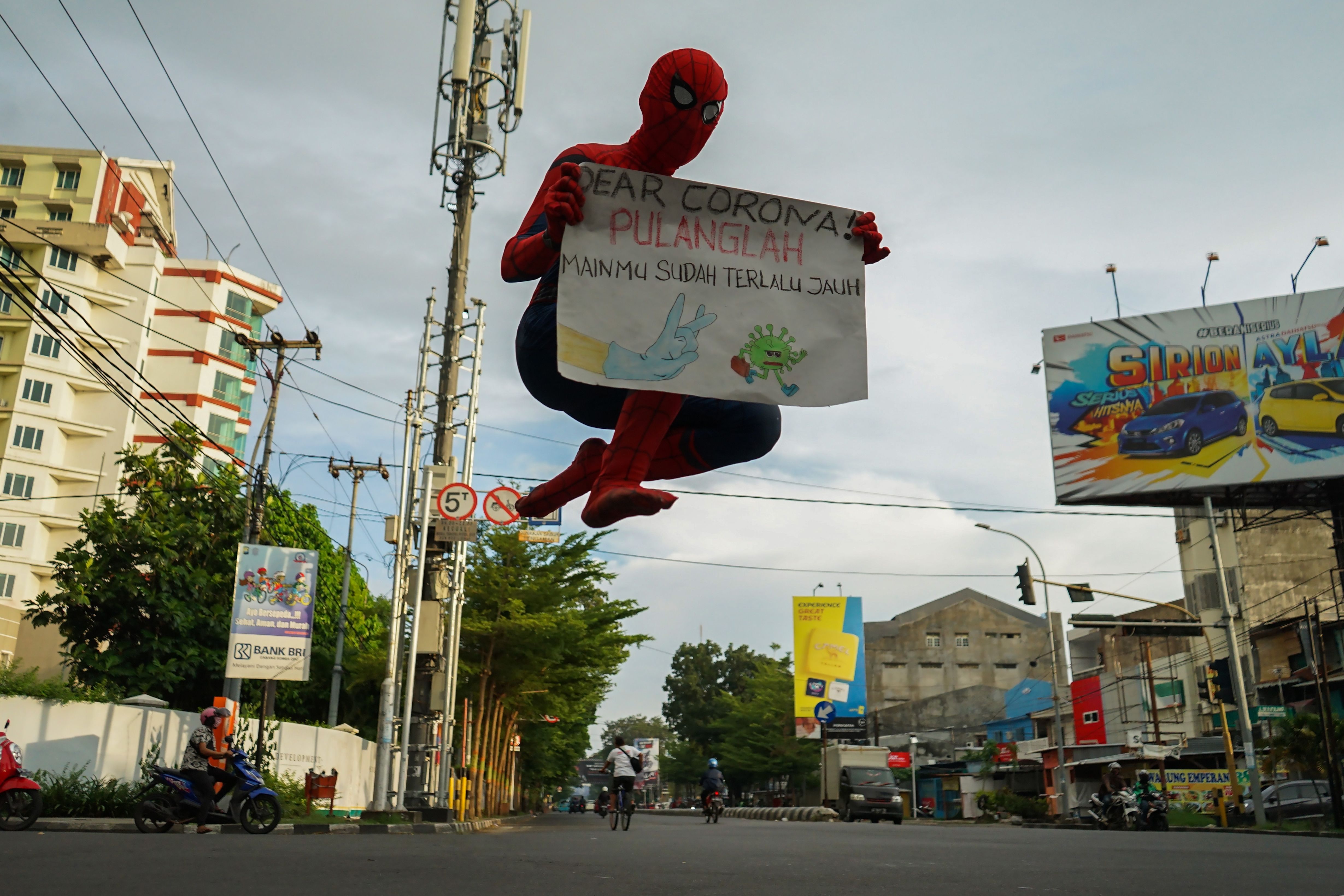Pria berpakaian superheo membawa poster tentang covid-19 di Makassar, Sulawesi Selatan, hari ini.