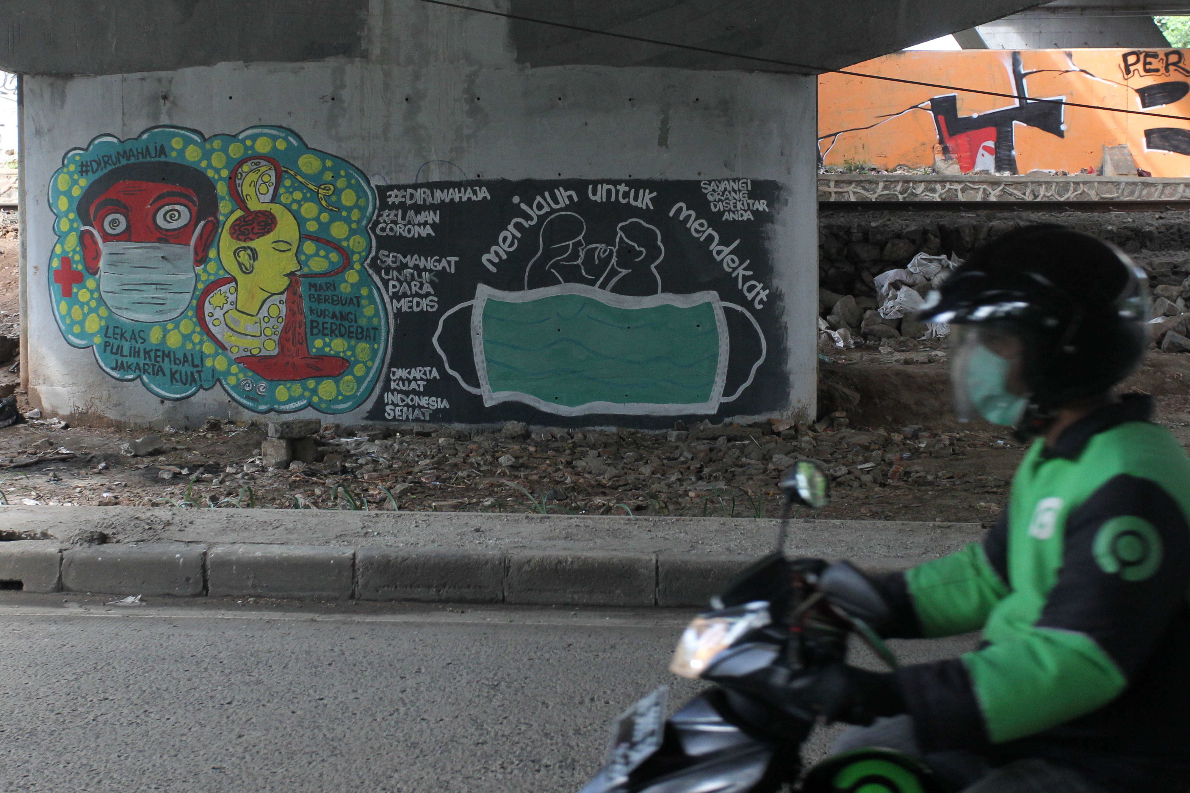 Warga melintas di depan mural ajakan untuk menggunakan masker dan tetap di rumah di kolong Jalan Rasuna Said, Jakarta, Rabu (1/4).