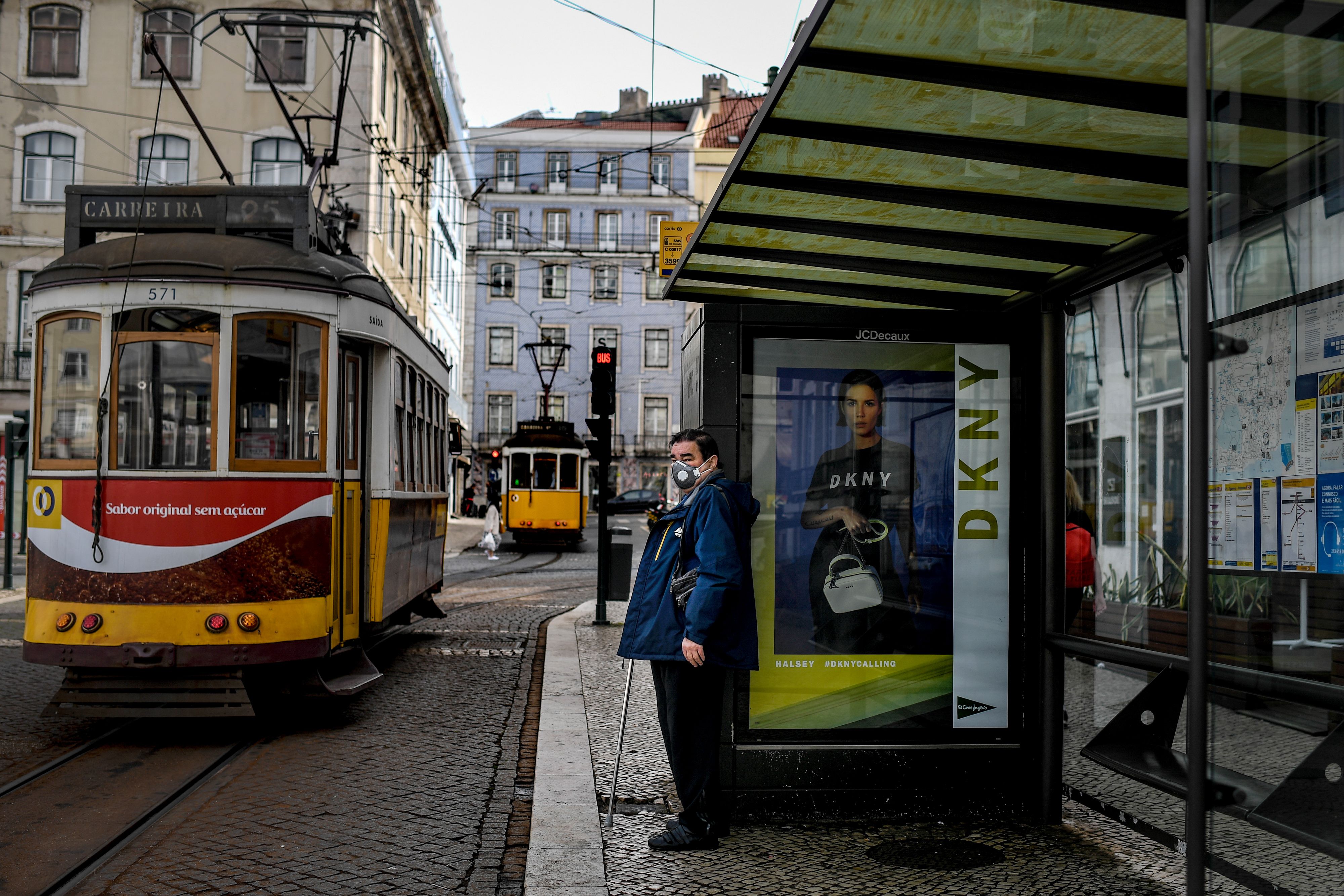 Seorang pria mengenakan masker sedang menunggu tram di Lisabon, Portugal.