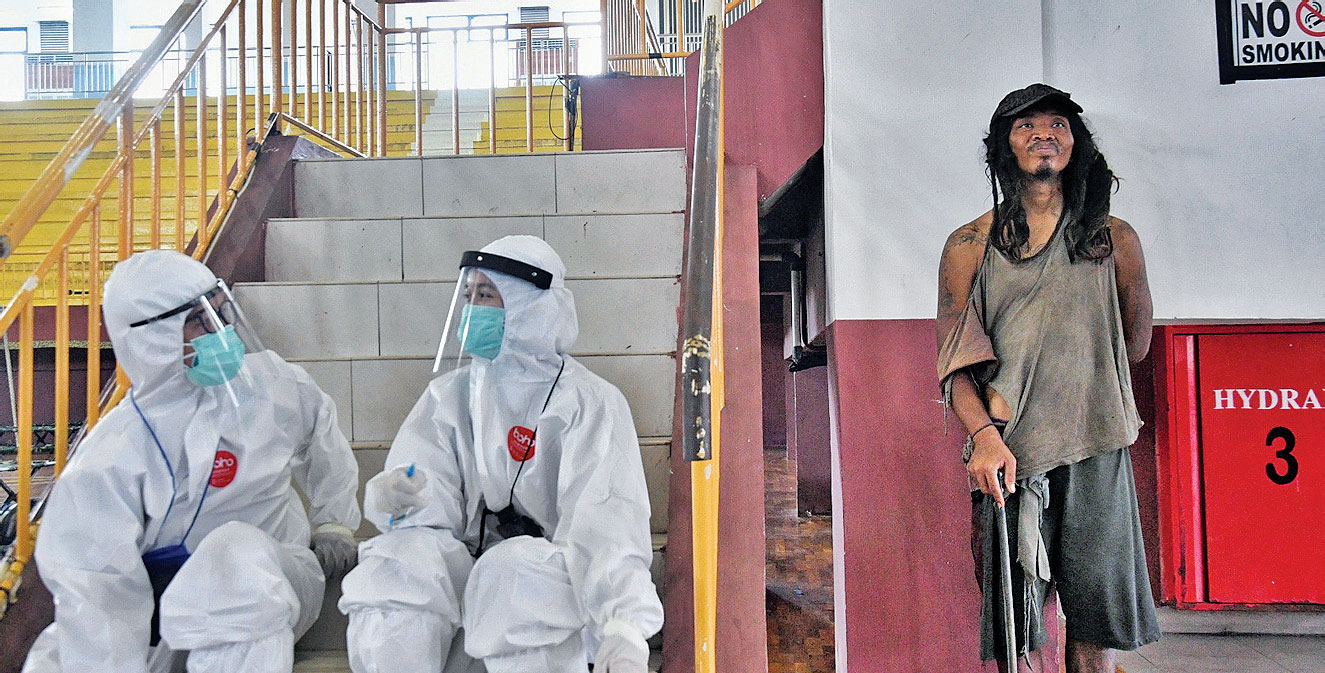 PENAMPUNGAN TUNAWISMA DAN PMKS: Dua tenaga medis mengenakan APD berbincang di samping seorang tunawisma di GOR Ciracas, Jakarta Timur 