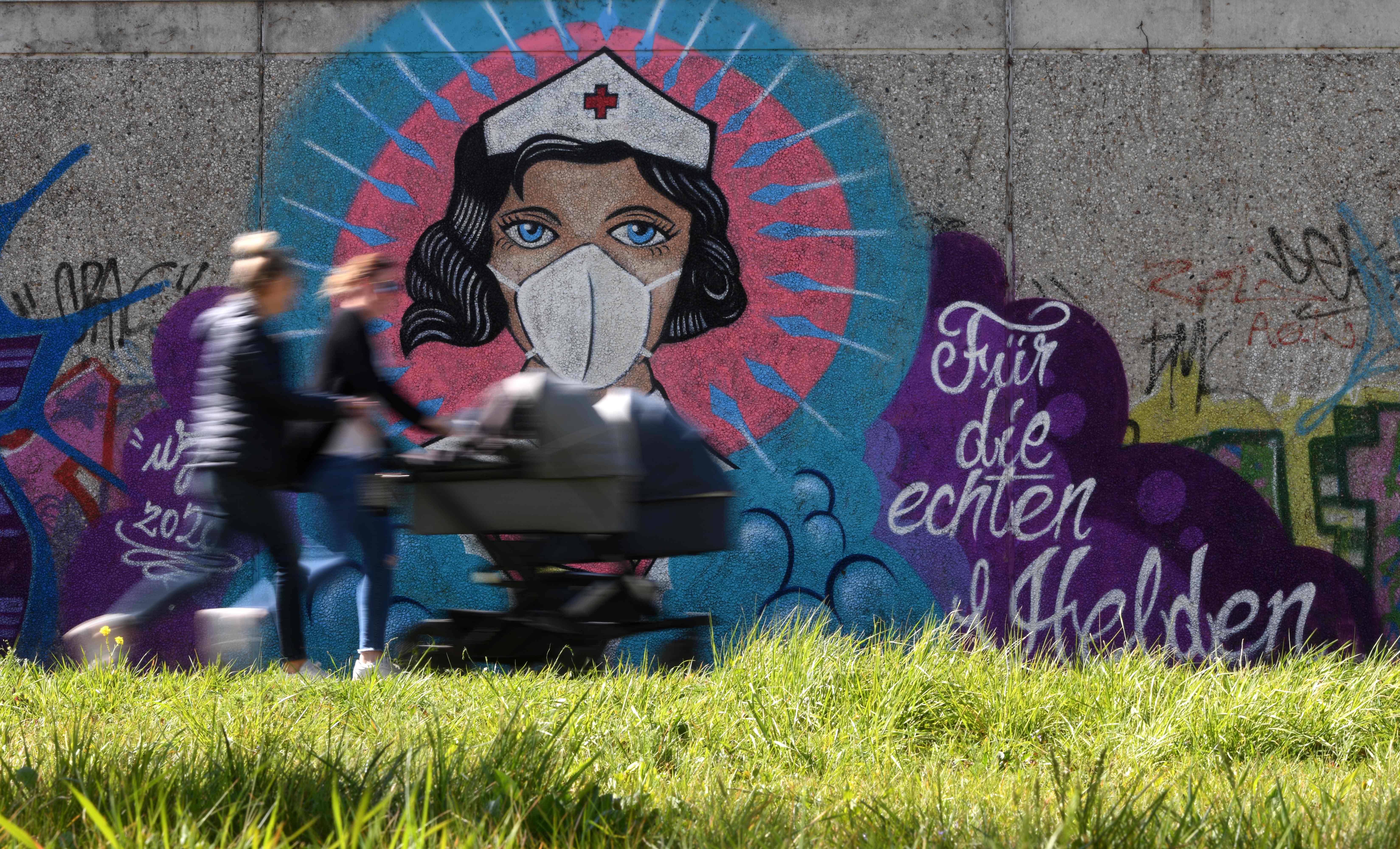 Warga Jerman melintasi grafiti perawat yang digambarkan sebagai superwoman ketika negara itu dihantam pandemi covid-19.