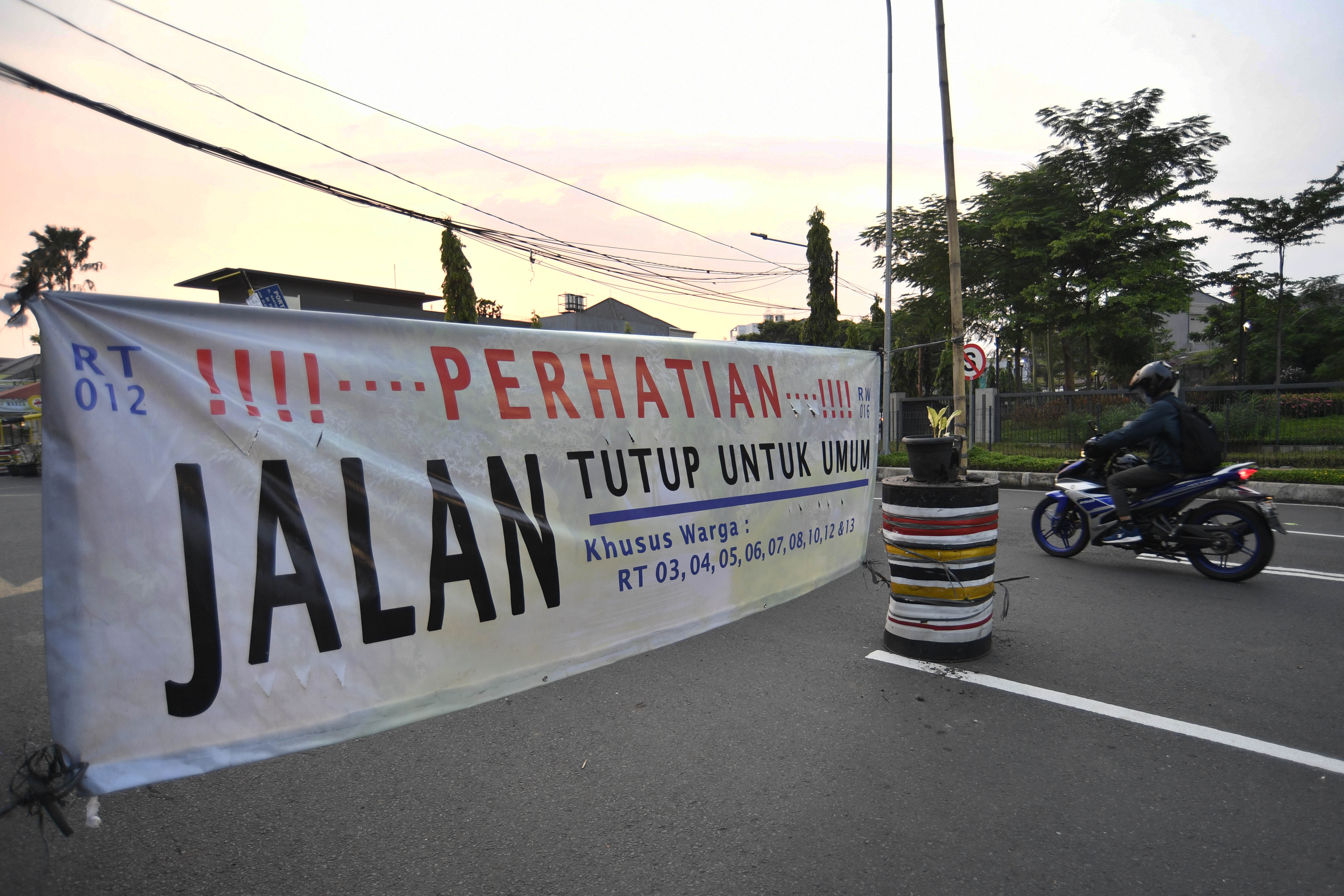 Pengendara sepeda bermotor melintasi spanduk penutupan jalan di kawasan Pondok Pinang, Jakarta.