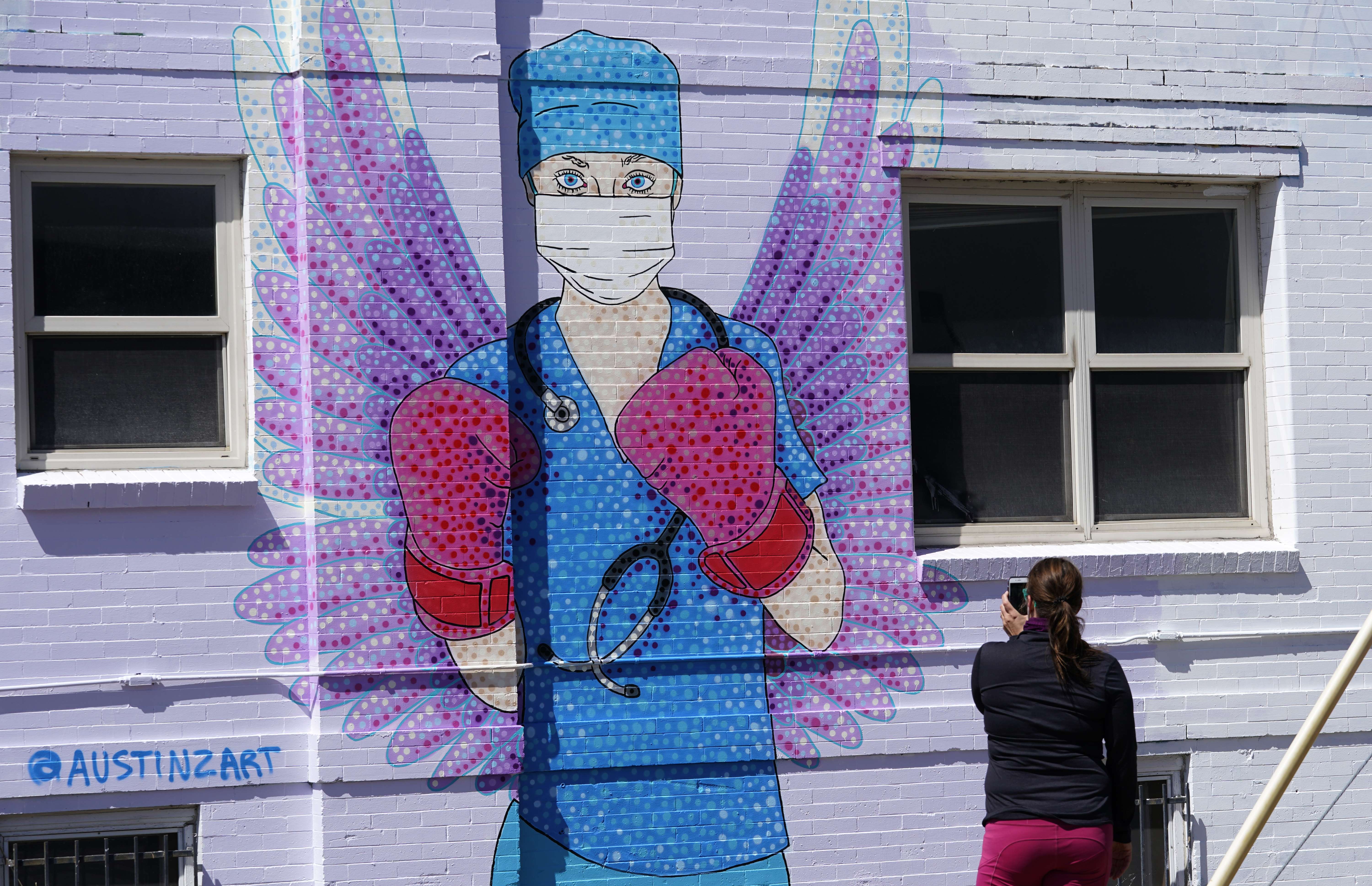 Seorang perempuan memotret mural tenaga medis di Denver, AS, yang dianggap sebagai pejuang covid-19.