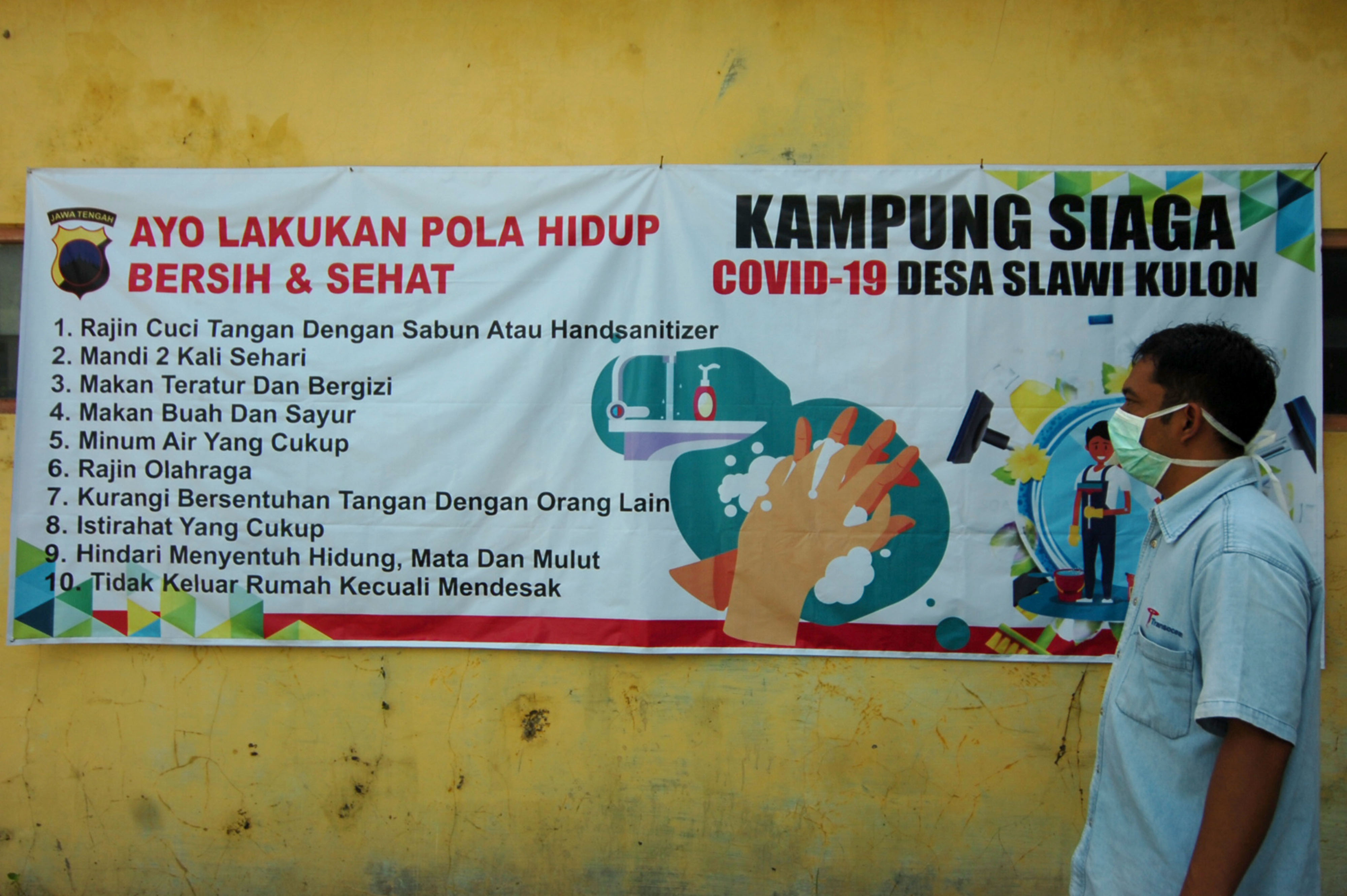 Seorang warga berjalan di depan spanduk saat pencanangan Kampung Siaga COVID-19 di Desa Slawi Kulon, Tegal, Jawa Tengah, Senin (13/4) lalu.