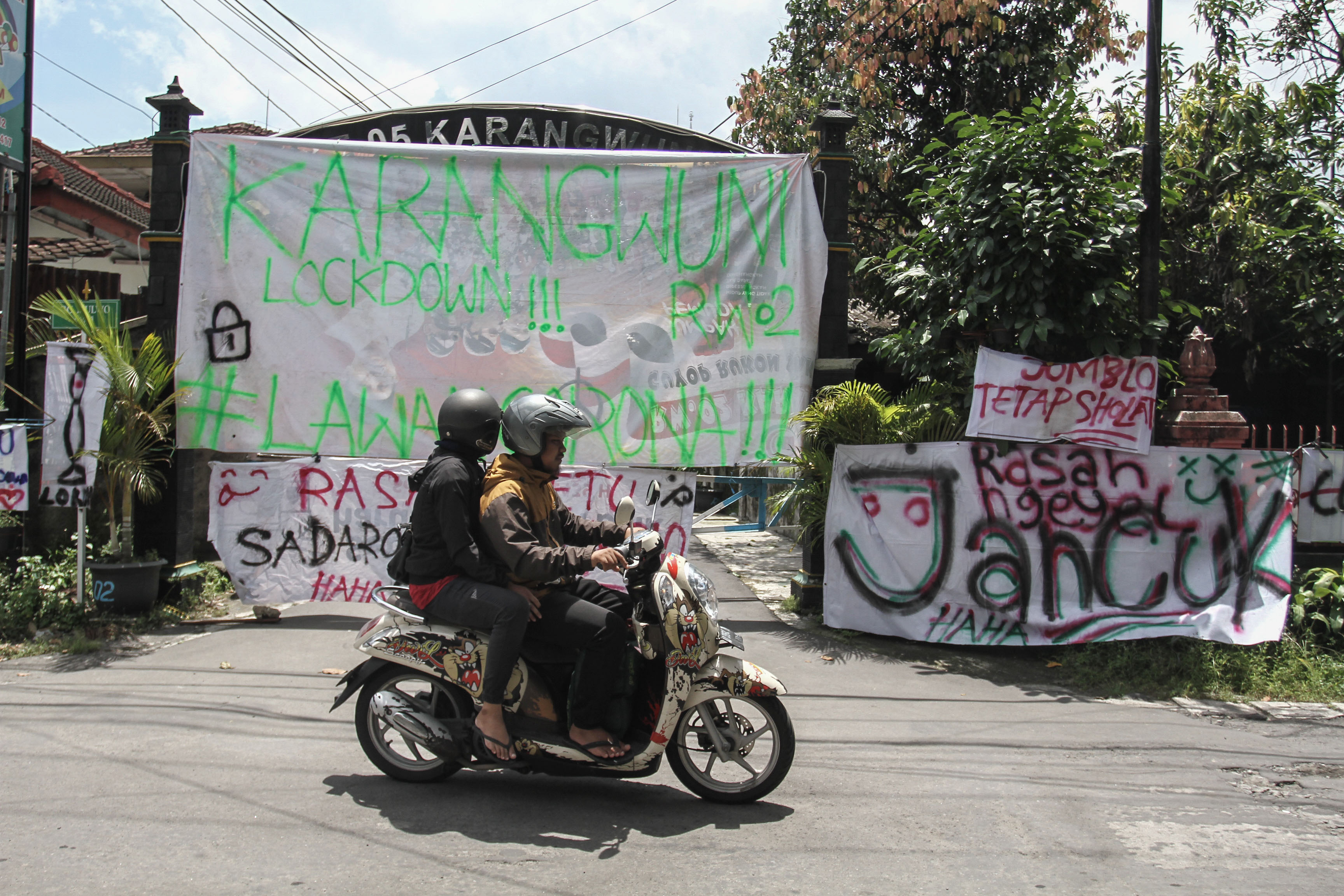 Warga melintas di depan spanduk penutupan jalan masuk Desa Karangwuni, Depok, Sleman, DI Yogyakarta (30/3).
