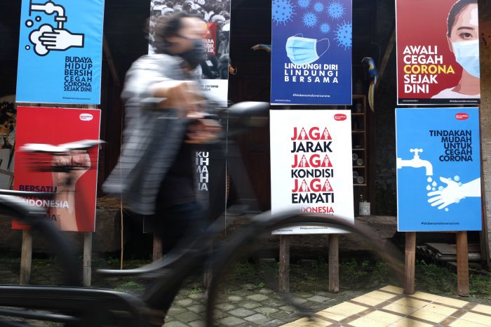 Warga melintasi sejumlah poster terkait upaya melawan covid-19 di Solo, Jawa Tengah