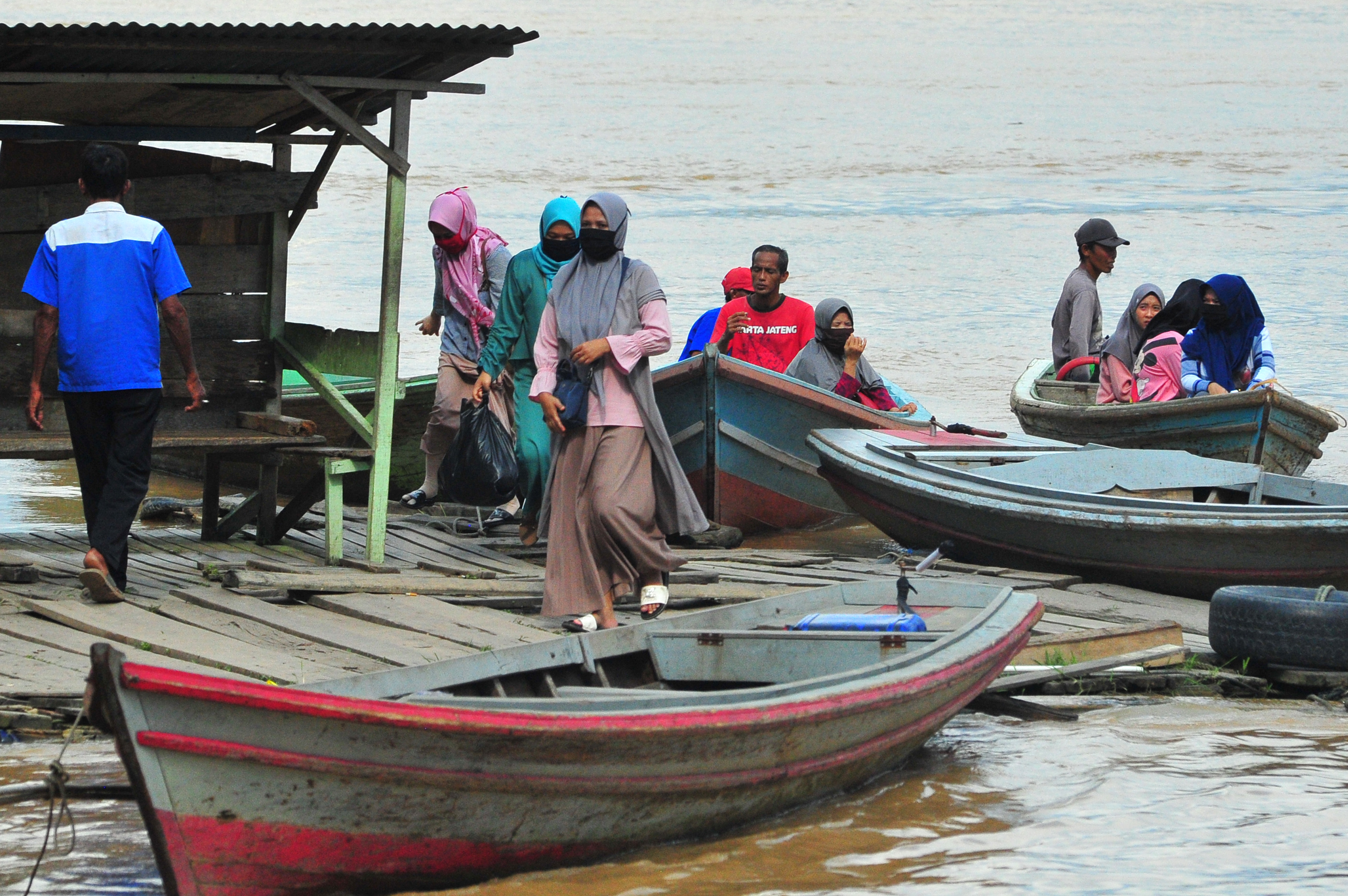 Warga mengenakan masker turun dari perahu penyeberangan di tepi Sungai Batanghari, Pelayangan, Jambi, Jumat (10/4). 