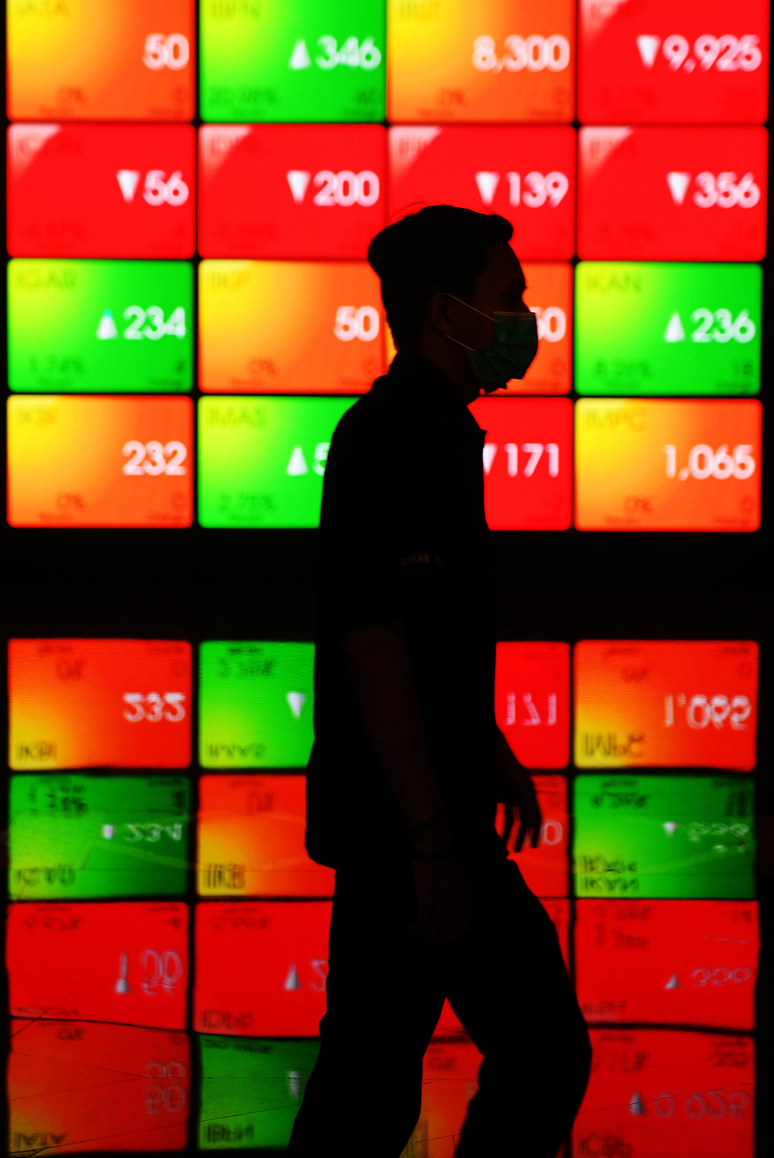Seorang pria melintasi layar elektronik pergerakan saham di Jakarta, Selasa (7/4/2020).