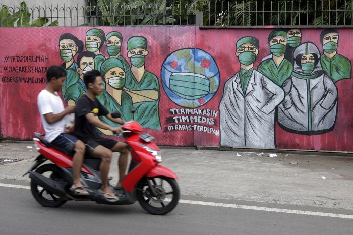 Pengendara motor melintas di depan mural tentang pandemi virus korona di Jalan Raya Jakarta-Bogor, Depok.