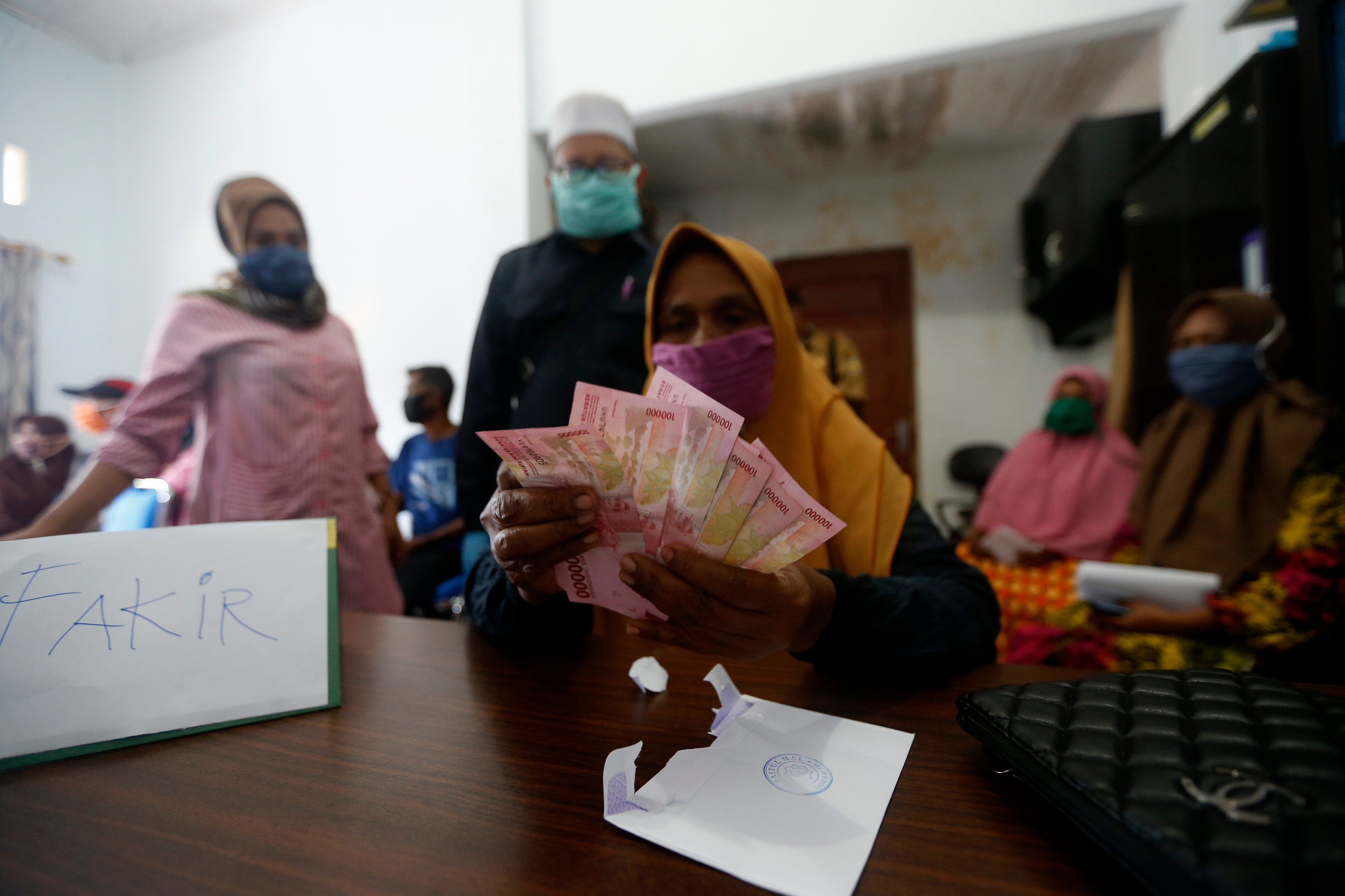 Warga penerima manfaat zakat dari lembaga Baitul Mal Kota Banda Aceh menghitung dan memperlihatkan uang yang baru diterima.