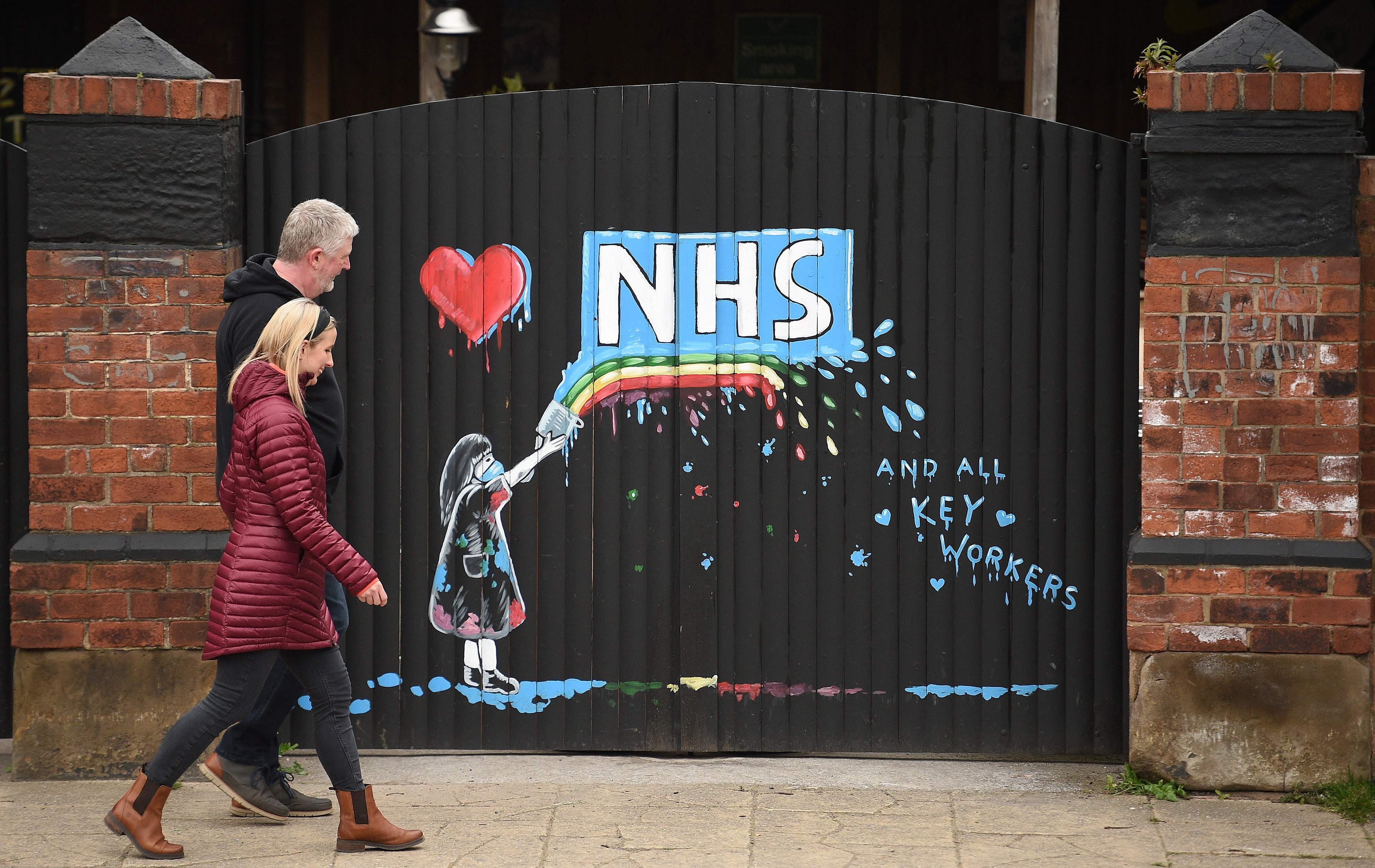 Sepasang warga berjalan di depan grafiti dukungan untuk NHS di Pontefract, Inggris.