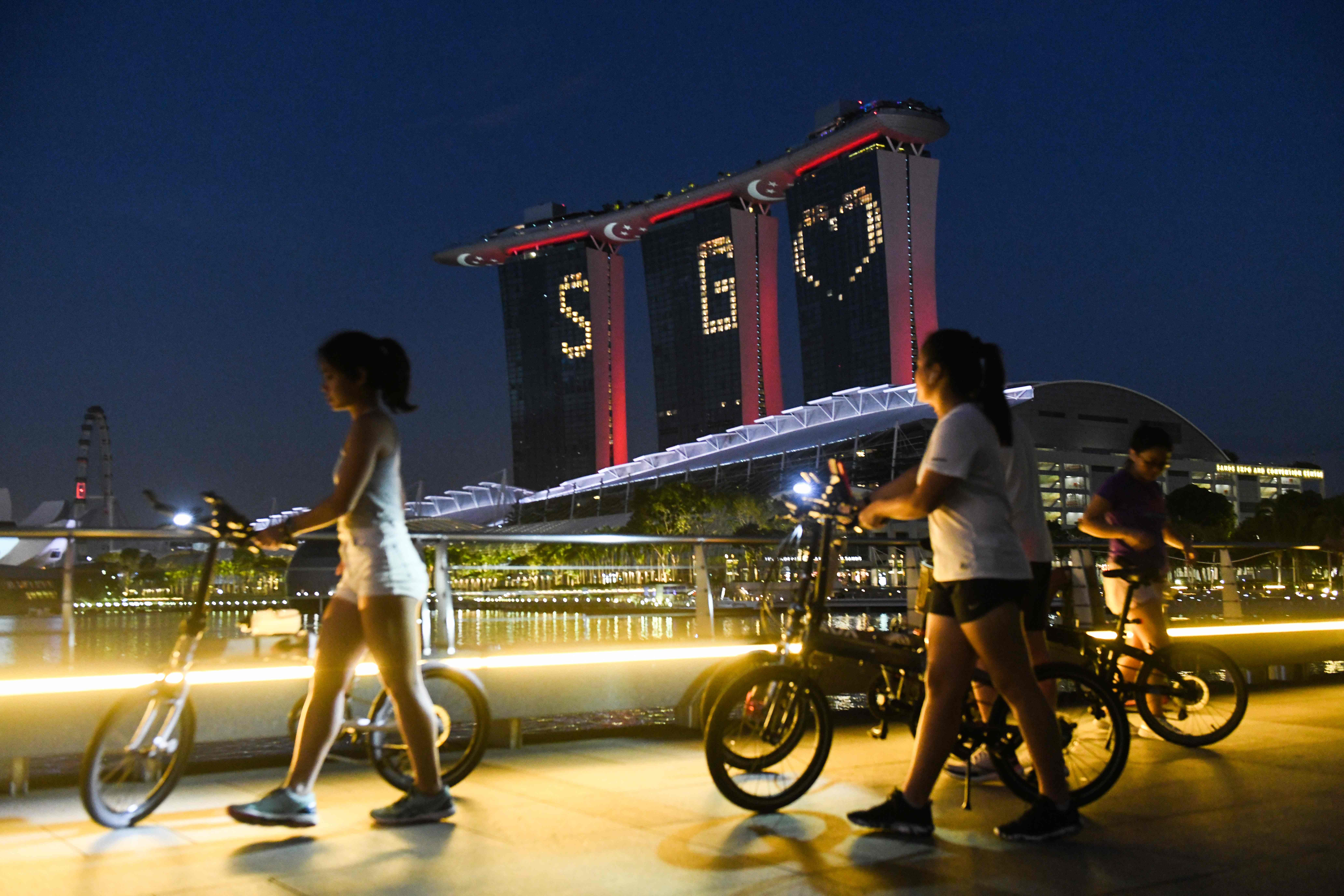 Warga melintas di depan Hotel Marina Bay Sands, Singapura yang menampilkan lampu bertuliskan SG dan logo hati.