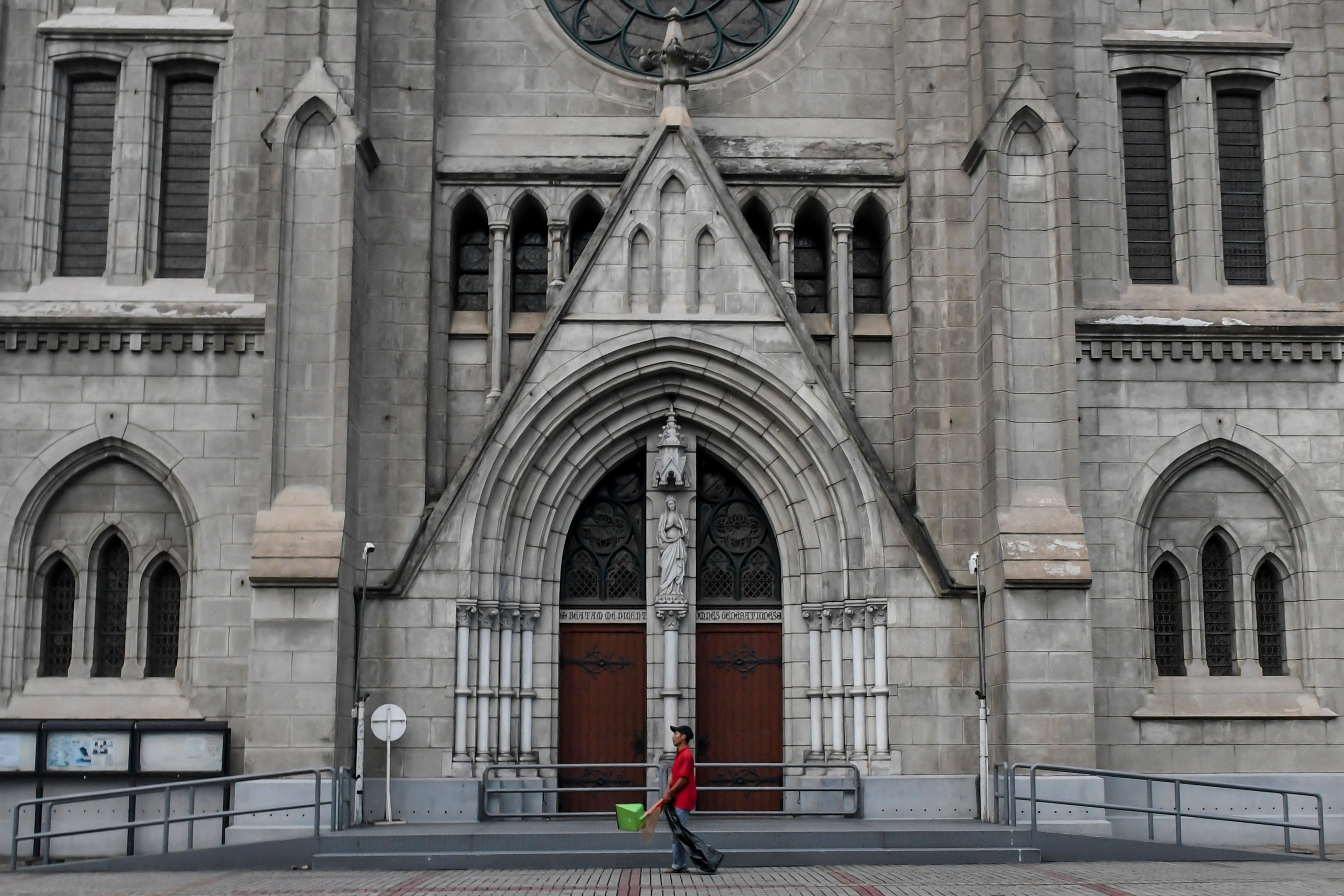 Petugas kebersihan melintas di depan pintu Gereja Katedral yang ditutup untuk umum, Jakarta, Minggu (5/4).