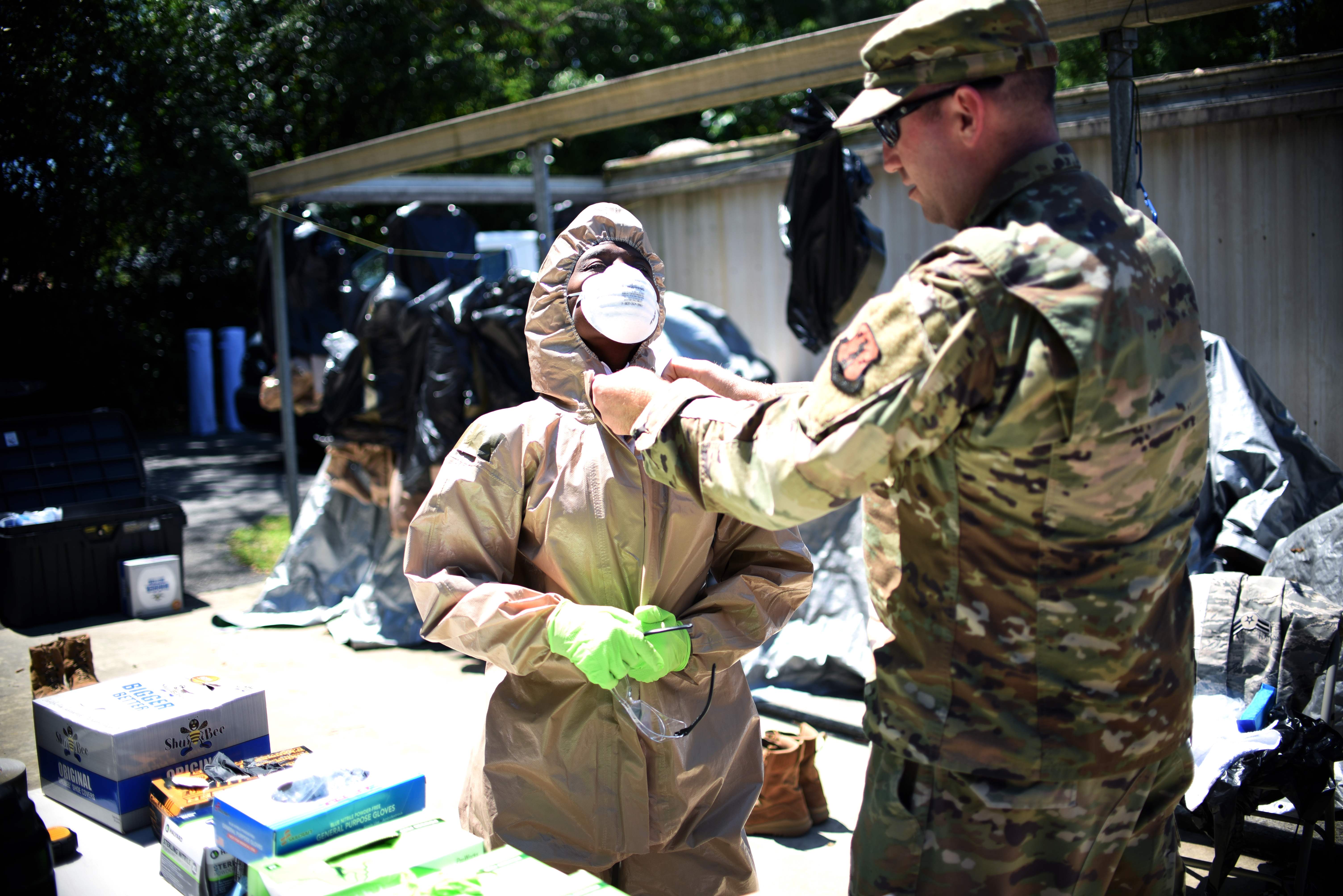 Seorang personel militer AS membantu rekannya mengenakan APD.