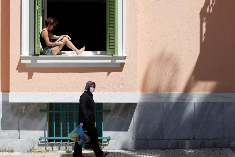 Seorang wanita duduk di jendela sambil membaca buku  saat karantina wilayah di Athena, Yunani, Jumat (17/4)