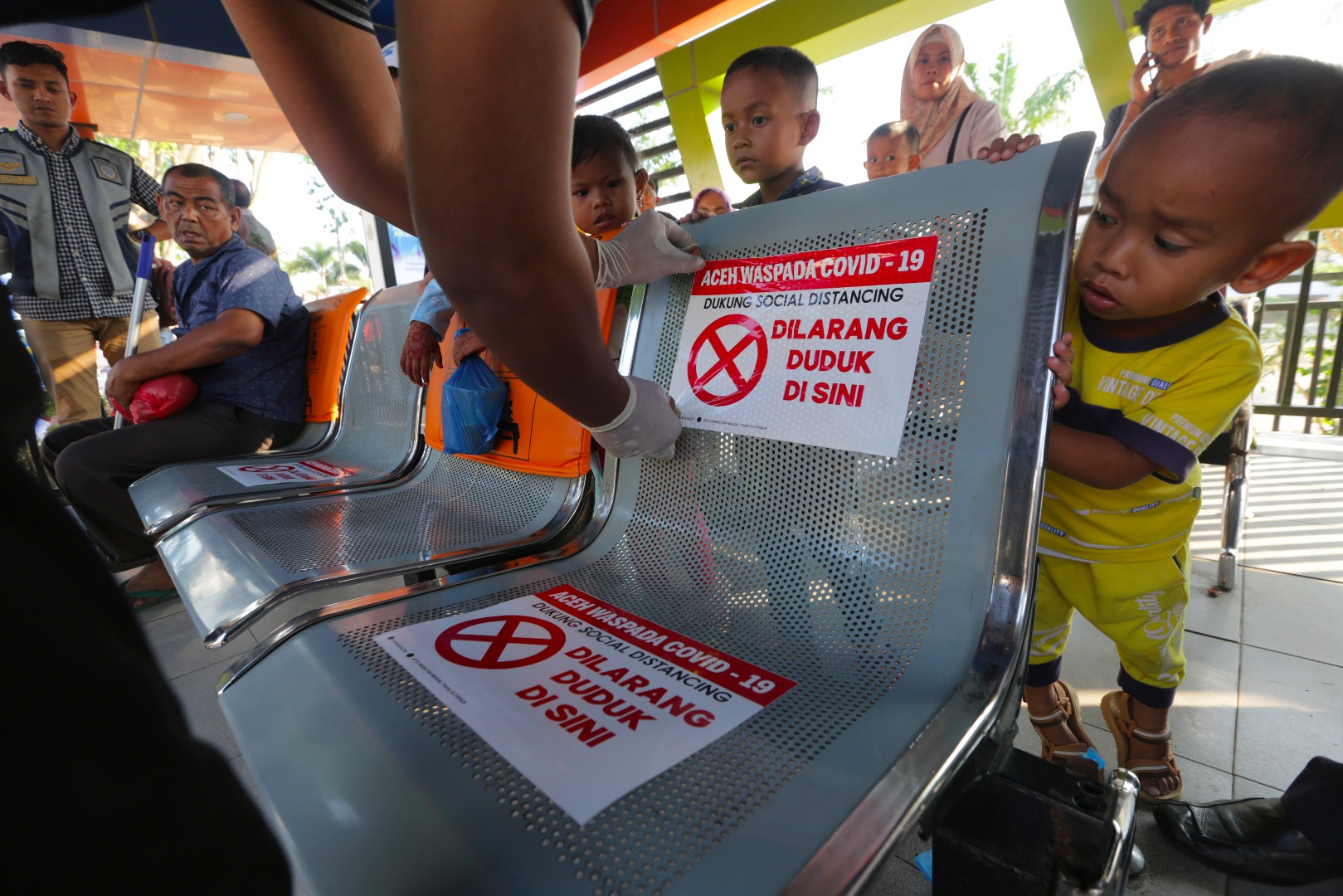 Seorang anak penasaran dengan stiker larangan duduk yang ditempel petugas di kursi halte bus.