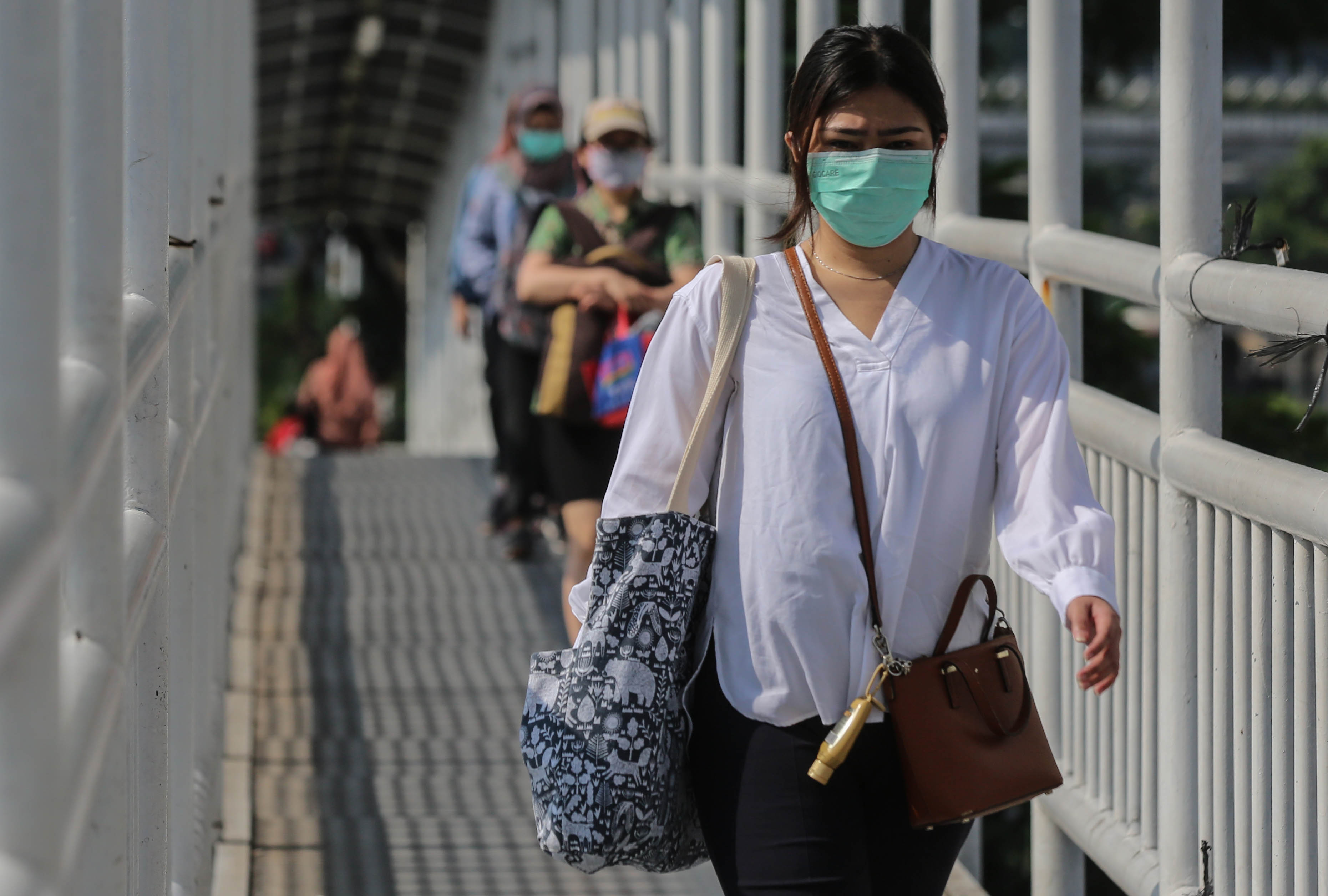 Warga mengenakan masker saat melintasi jembatan penyeberangan menuju halte bus Trans-Jakarta.