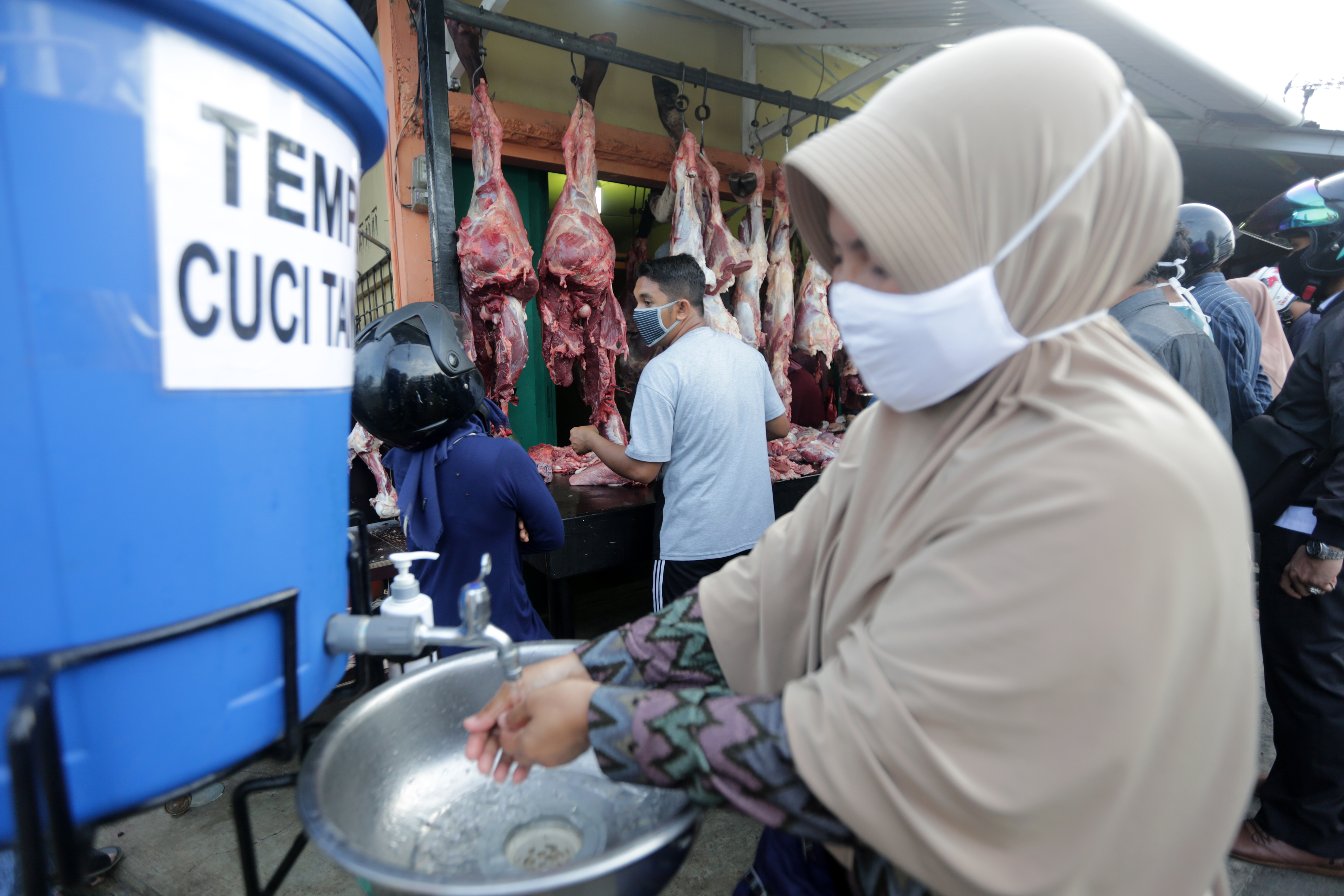Warga yang memakai masker mencuci tangan sesudah membeli daging di hari tradisi pemotongan hewan (meugang) di Beurawe, Banda Aceh, kemarin.