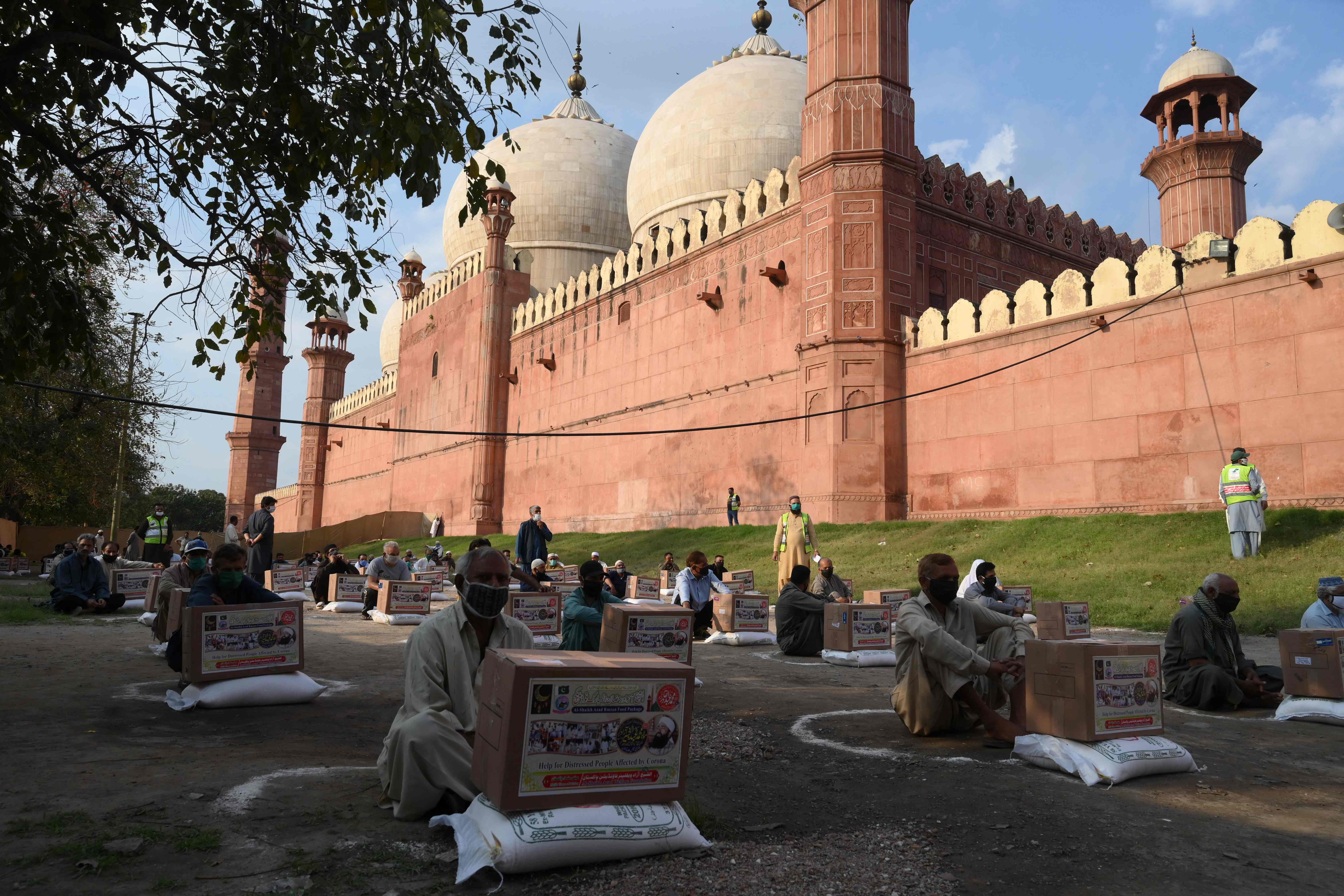 Warga duduk menjaga jarak sosial saat menerima bantuan makanan di Lahore, Pakistan.