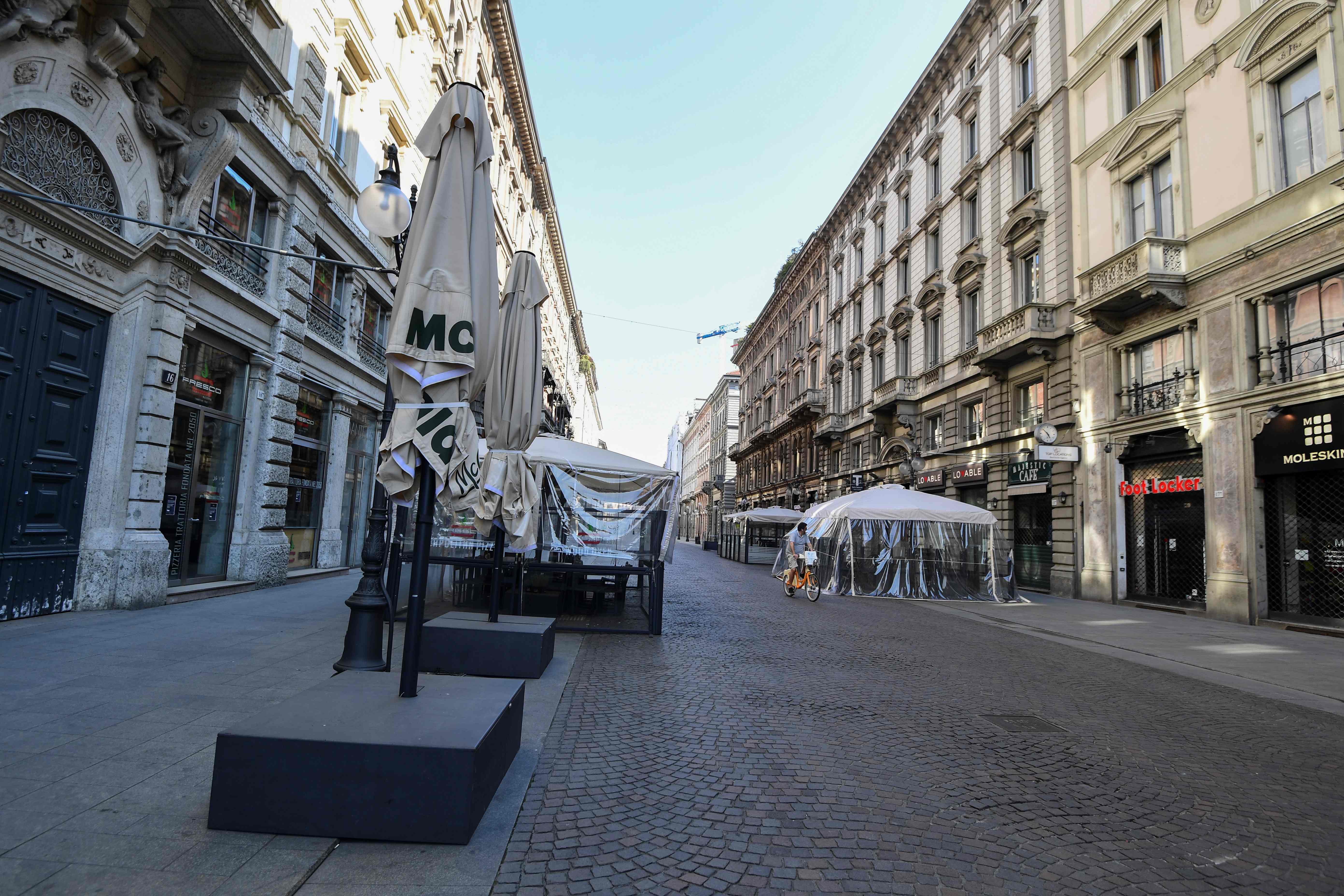 Seseorang tengah mengayuh sepedanya di sebuah jalan di kota Milan, Italia yang sepi. 