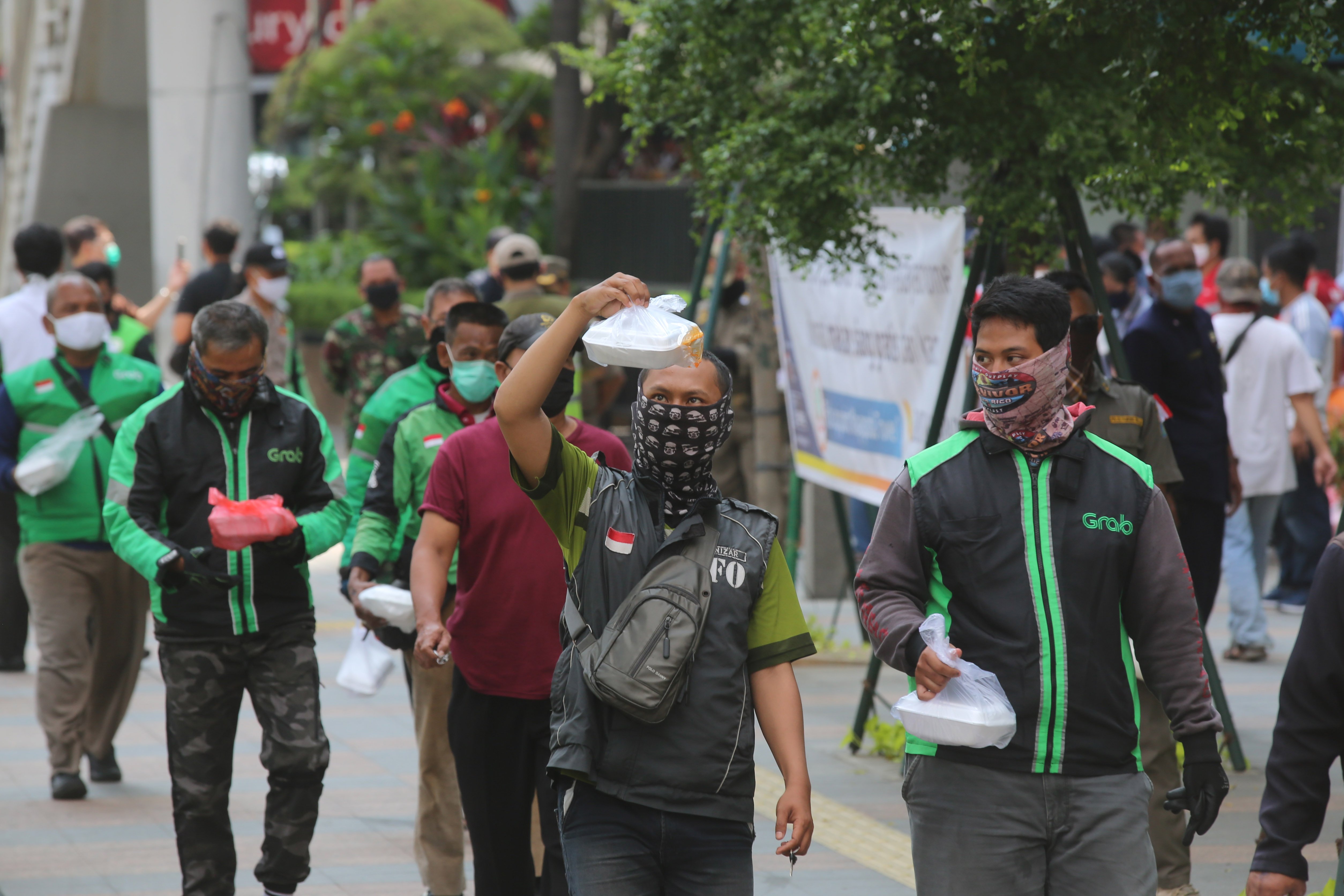 Pengemudi ojek daring bersama warga antre untuk mendapatkan makan siang dari salah satu perusahaan di Jakarta.