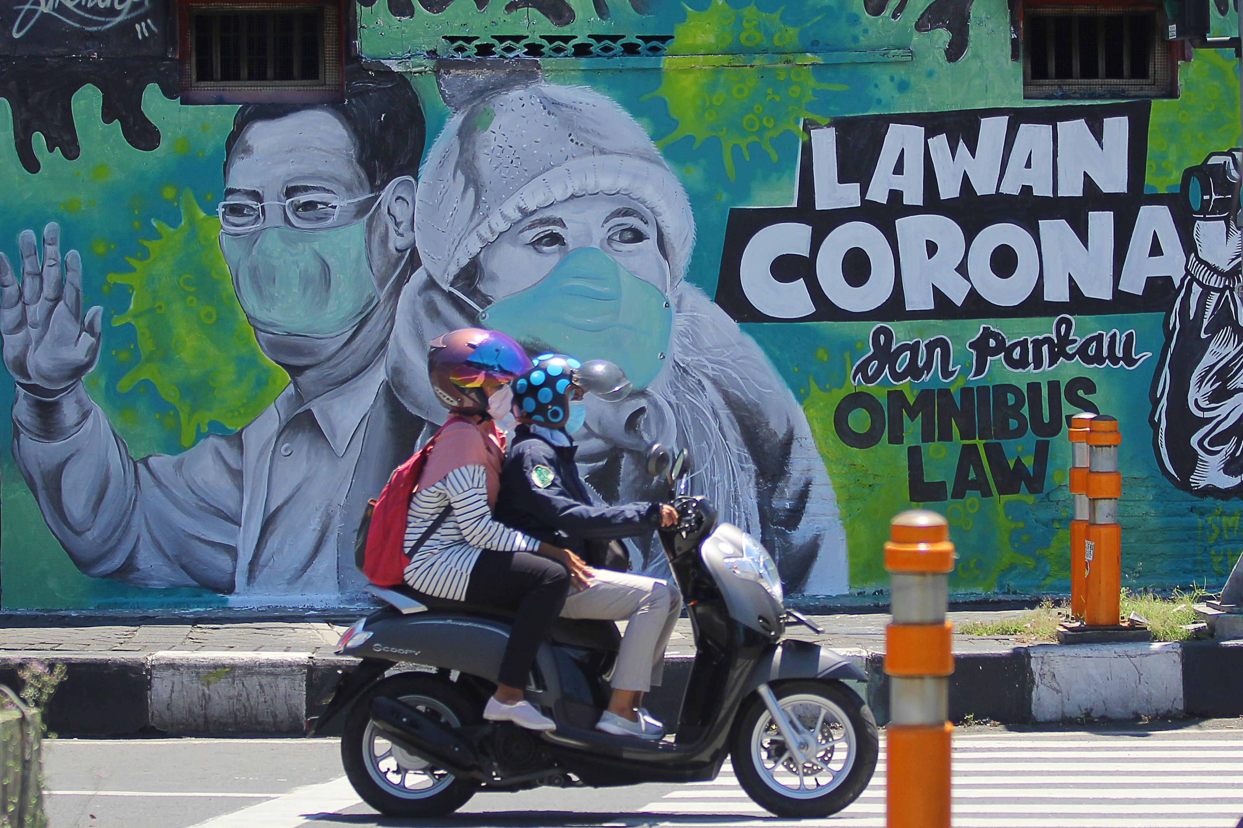 Pengendara motor melintasi mural terkait Covid-19 di Surabaya, Jawa Timur.