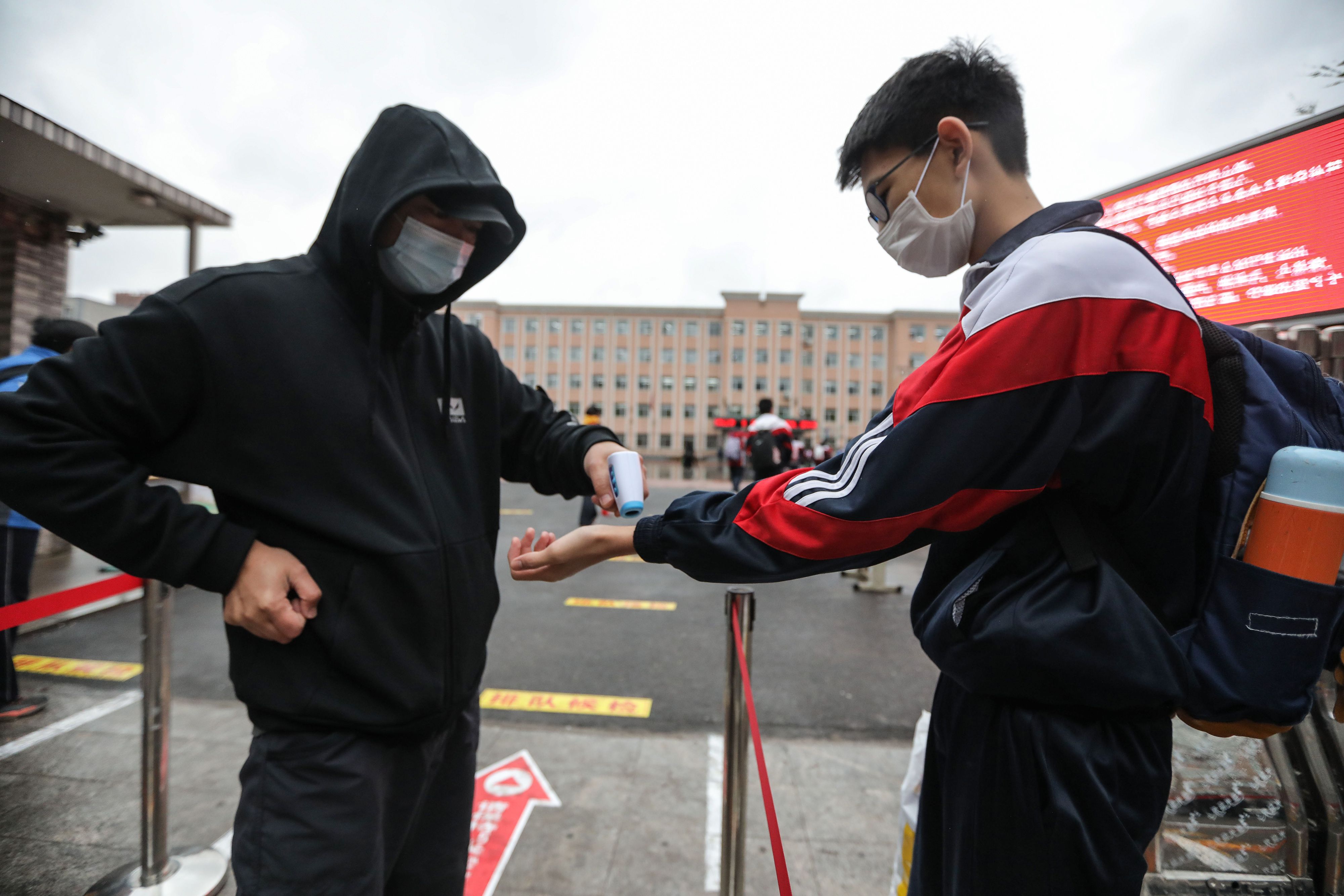 Petugas memeriksa suhu tubuh pelajar yang akan masuk sekolah setelah aktivitas belaja mengajar dibuka kembali di Shenyang, Tiongkok.