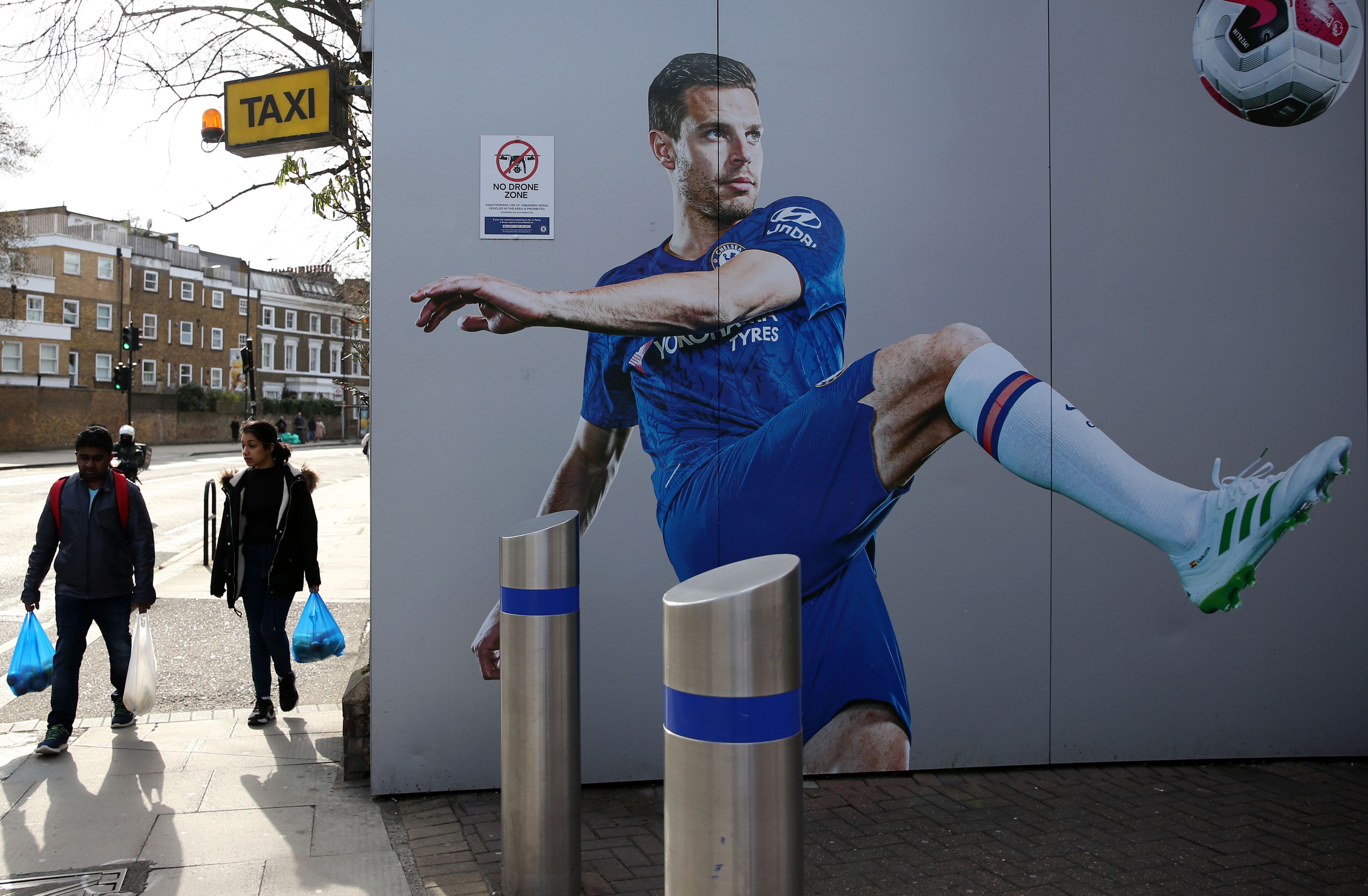 Pejalan kaki melewati mural pemain Chelsea di luar Stadion Stamford Bridge, London, Inggris.