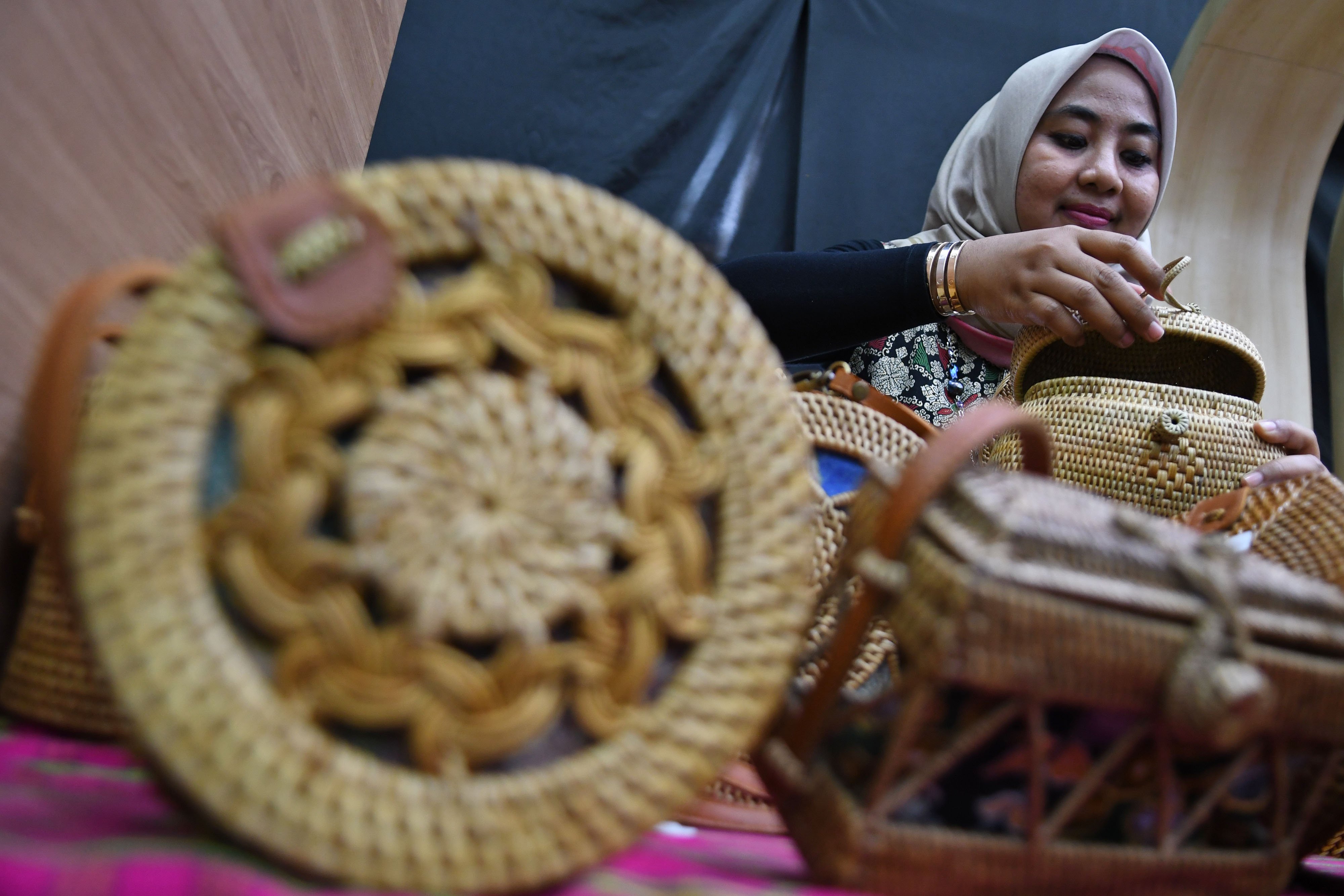 Perajin merapikan tas anyaman rotan buatannya yang tengah dipamerkan.