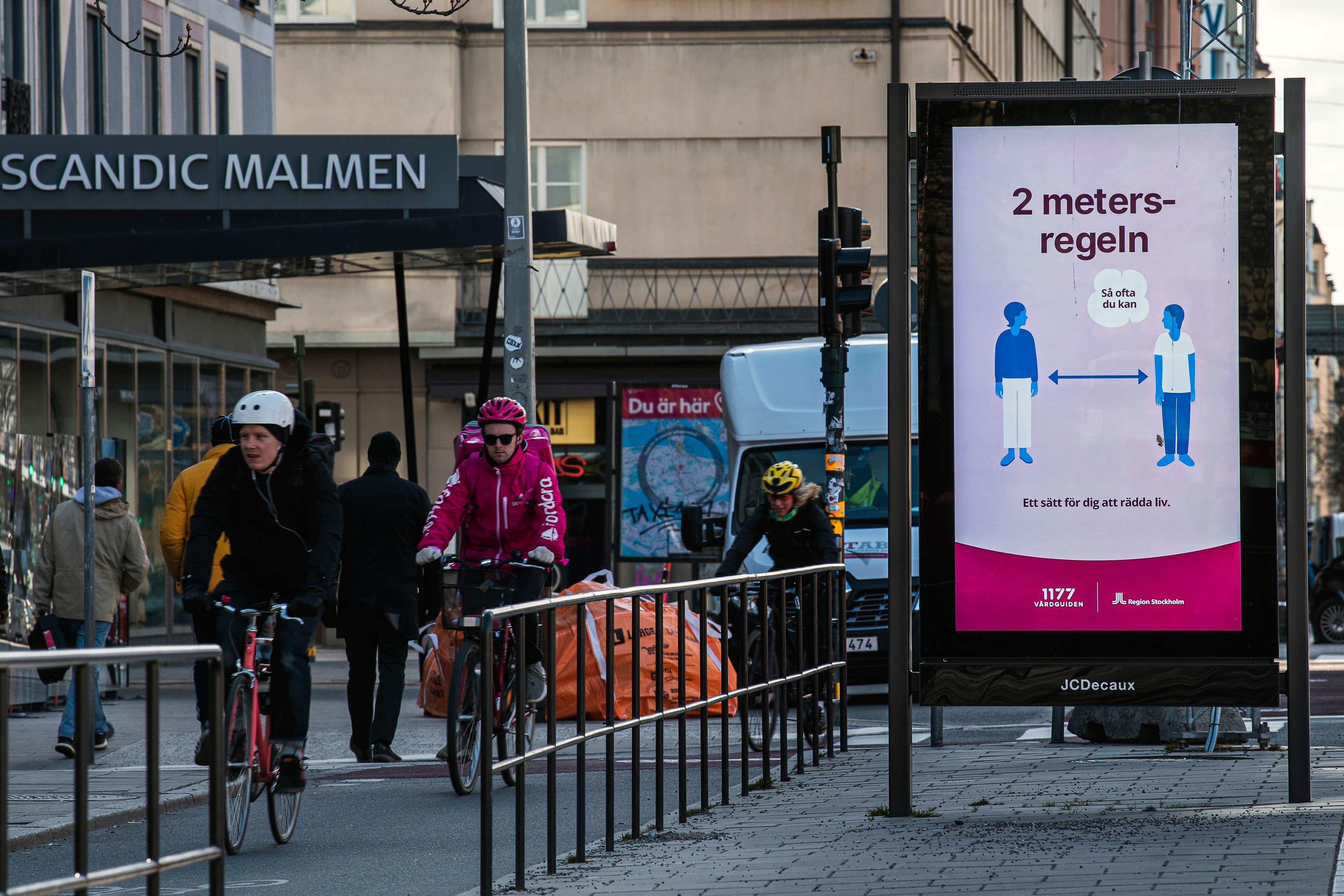 Pesepeda melintas di samping papan iklan yang mengingatkan warga untuk menjaga jarak di Stockholm, Swedia.