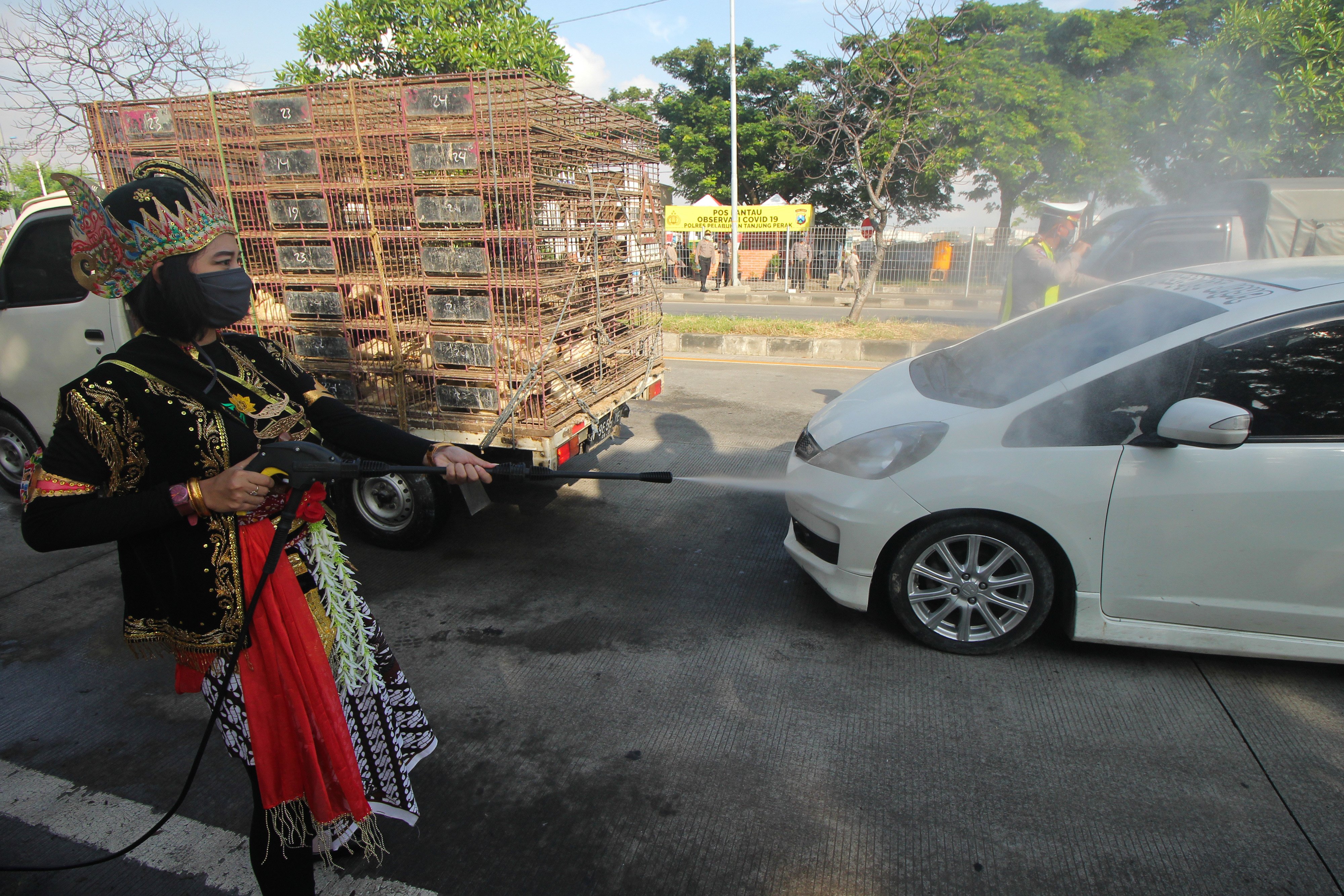 Polisi berpakaian tokoh wayang menyemprotkan larutan disinfektan ke kendaraan bermotor yang memasuki Surabaya di Jembatan Suramadu.