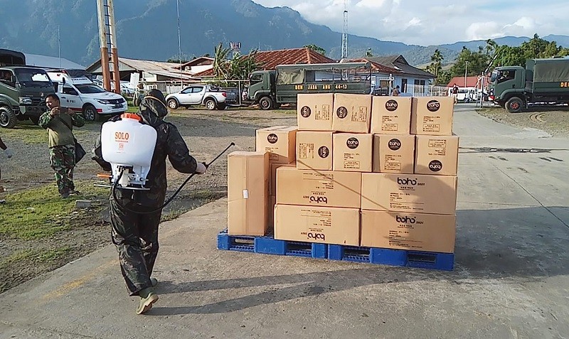 Ilustrasi -- Petugas menyemprotkan disinfektan pada kotak berisi bantuan APD di Papua. 