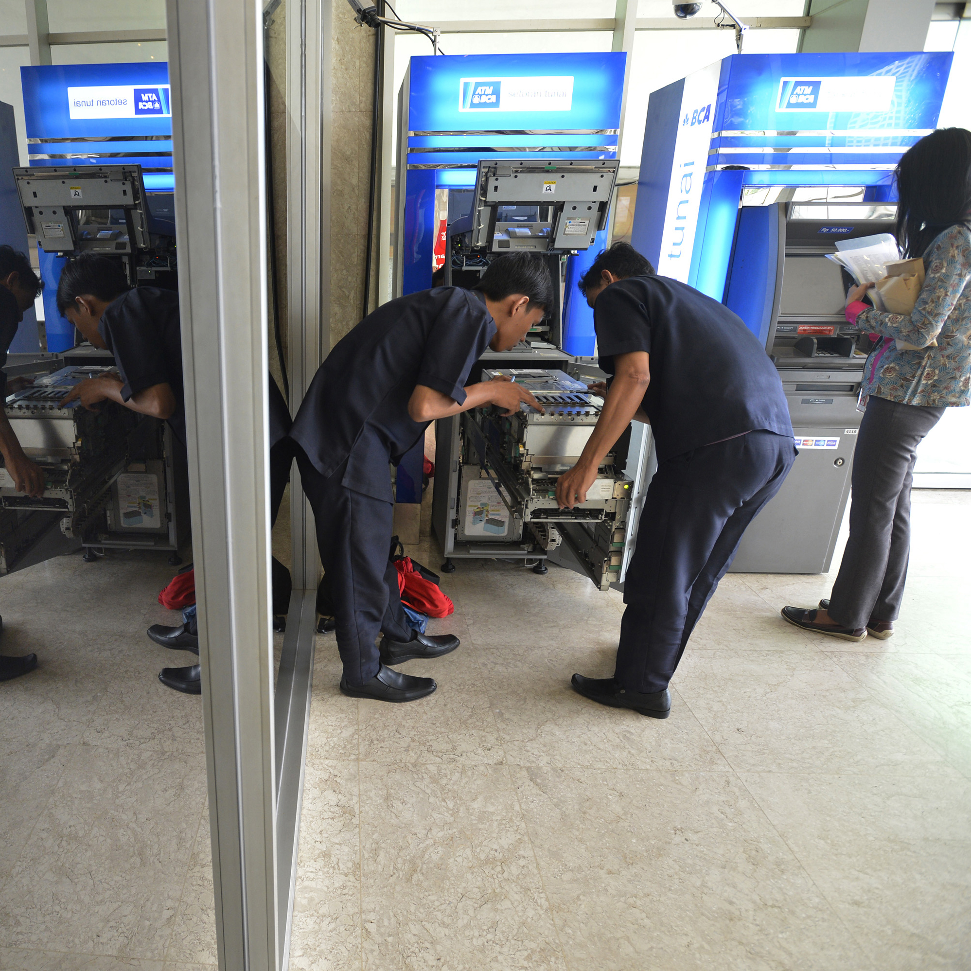 Petugas sedang memasukkan uang ke mesin ATM. 