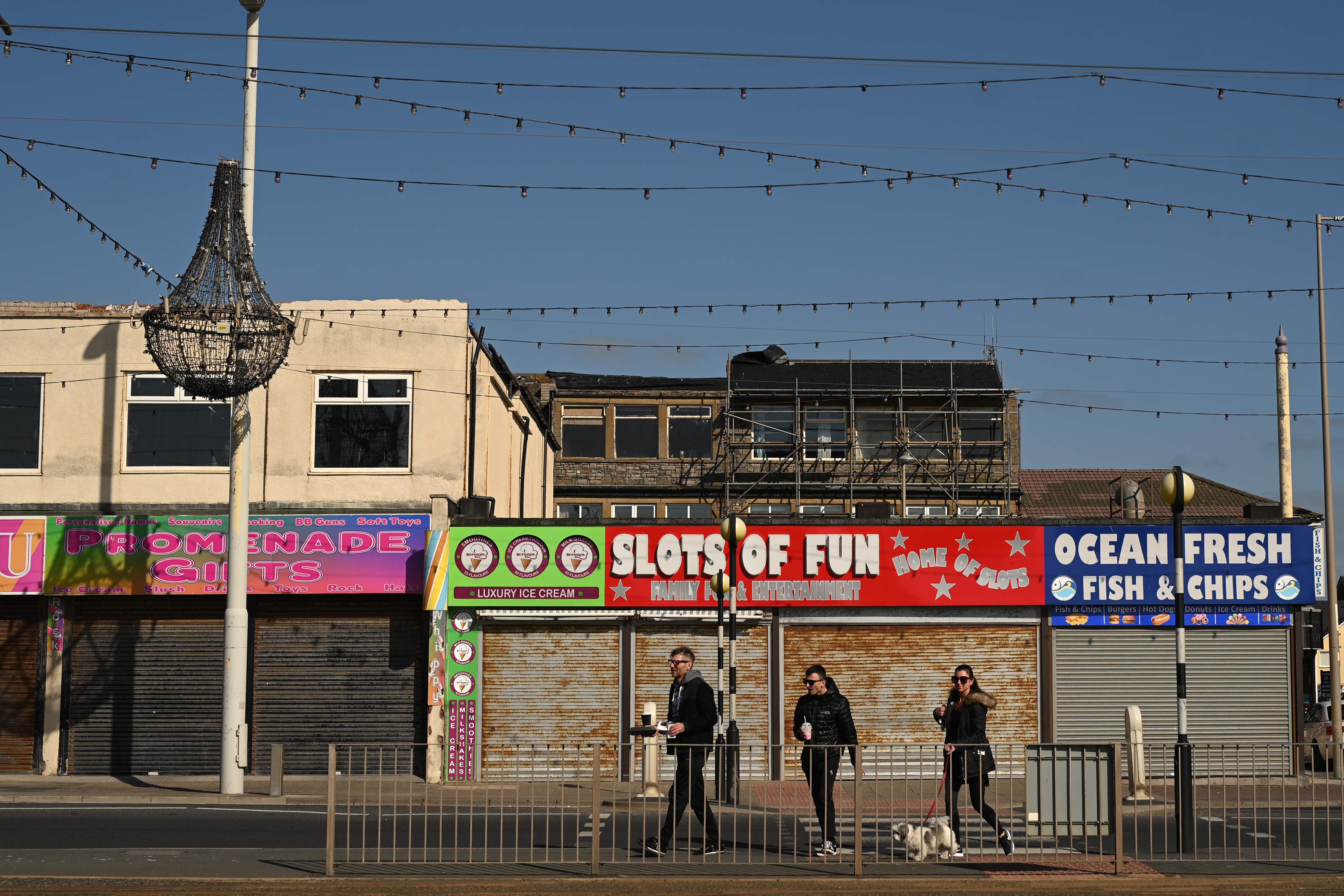 Warga melintas di depan rangkaian toko yang tutup akibat aturan lockdown di Blackpool, Inggris.