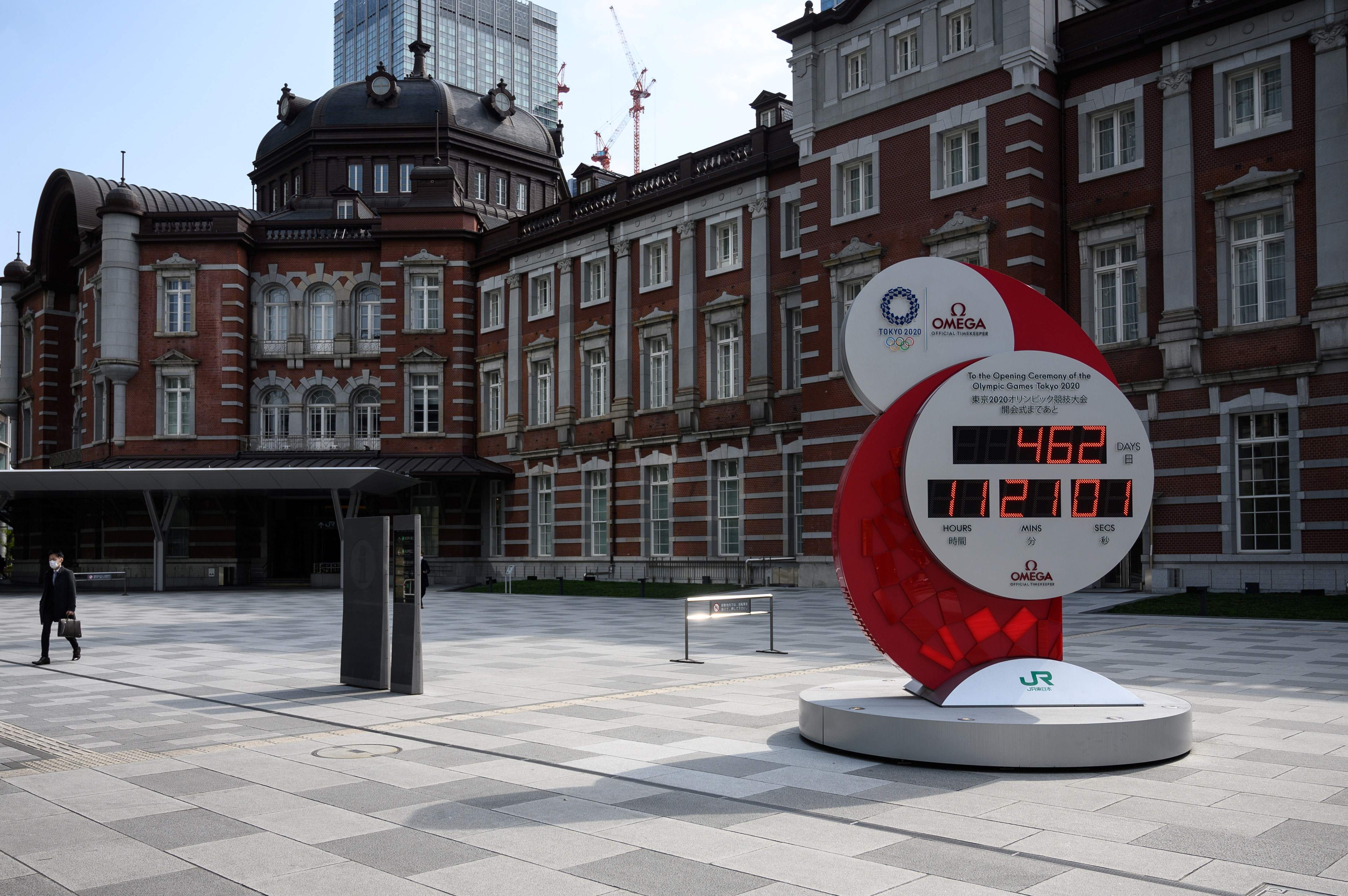 Seorang pria yang memakai masker berjalan di sebelah jam hitung mundur Olimpiade Tokyo 2020 di luar stasiun kereta api Tokyo, Kamis (17/4).