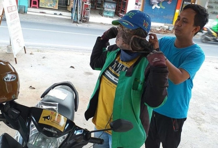 Pendiri Rumah Kreatif dan Pintar Muhammad Aripin (kanan) memakaikan masker kain ke salah satu pengemudi ojek online.