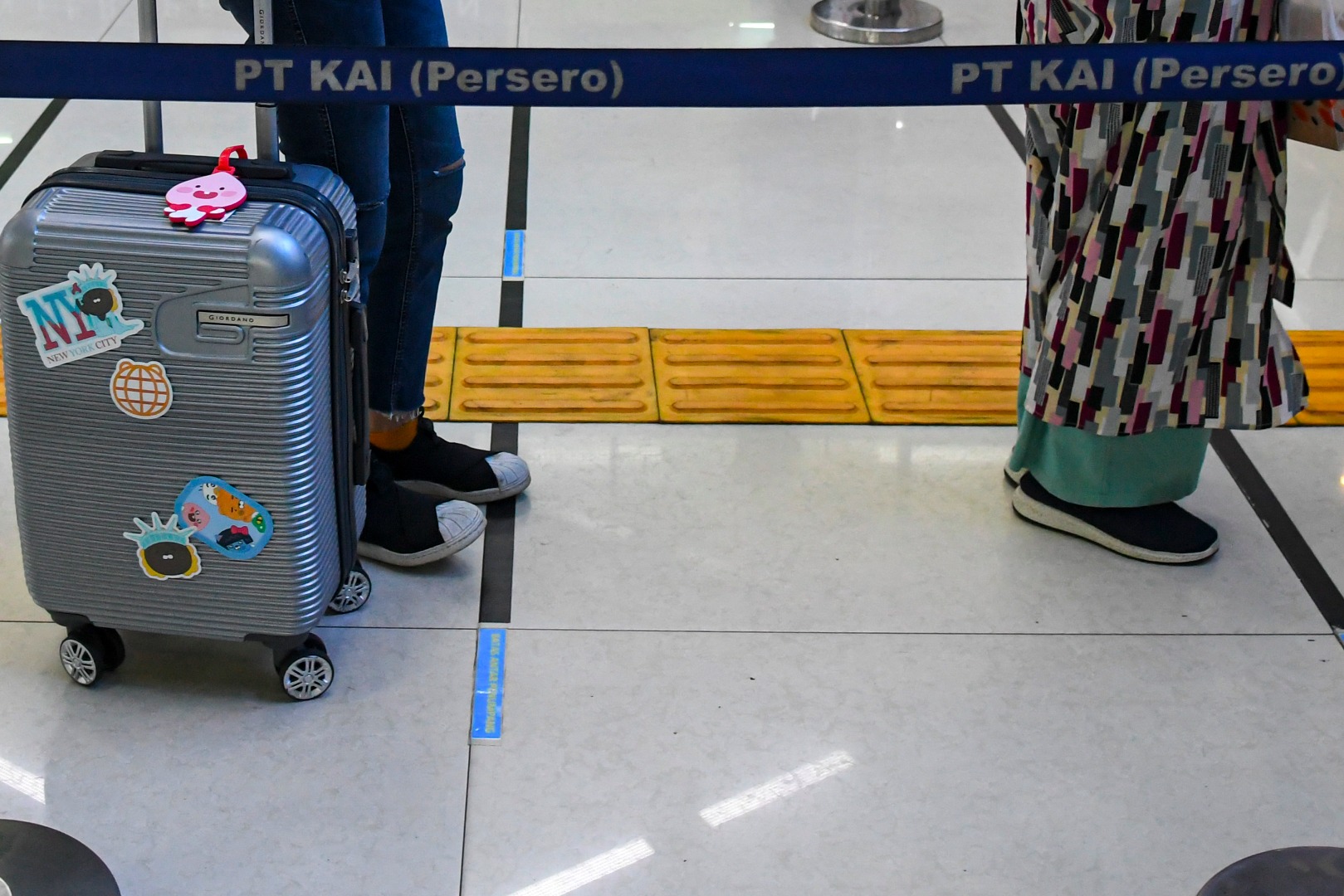  Calon penumpang antre pada pembatas stiker panduan tanda pengatur jarak sosial (social distancing) di Stasiun Gambir.