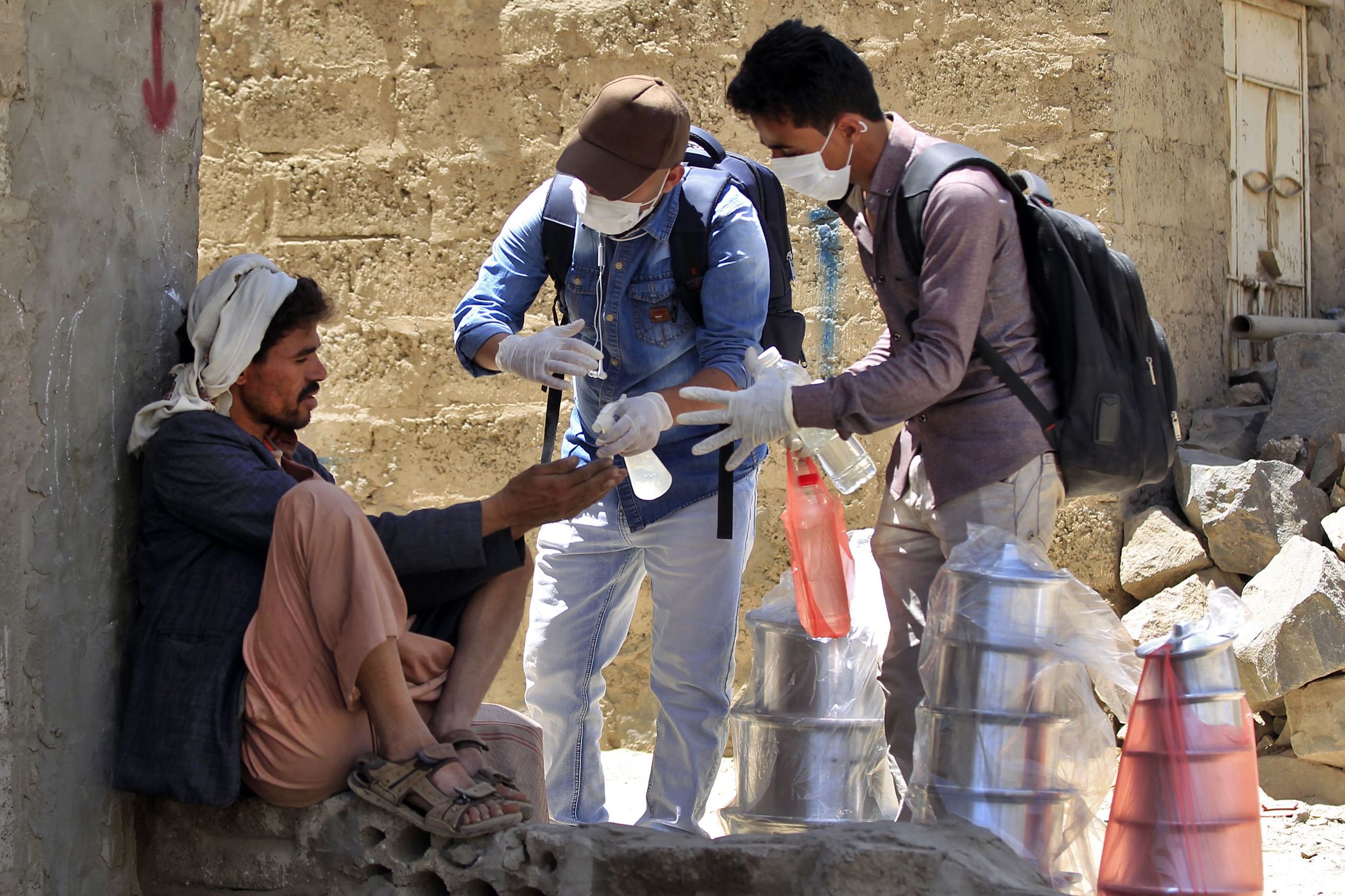 Sukarelawan Yaman menyemprotkan disinfektan ke tangan seorang pria di lingkungan miskin Sanaa.