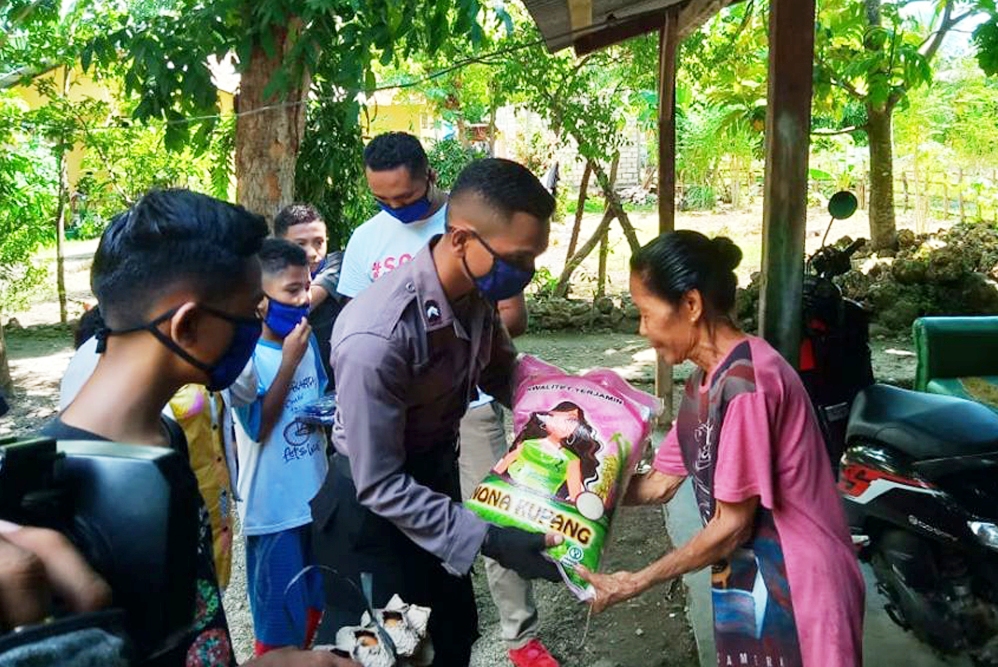 Anggota Polda Nusa Tenggara Timur (NTT) Bripda Nikolaus Irsan Tapobali, 19, menyerahkan bantuan sembako kepada warga yang terdampak virus ko