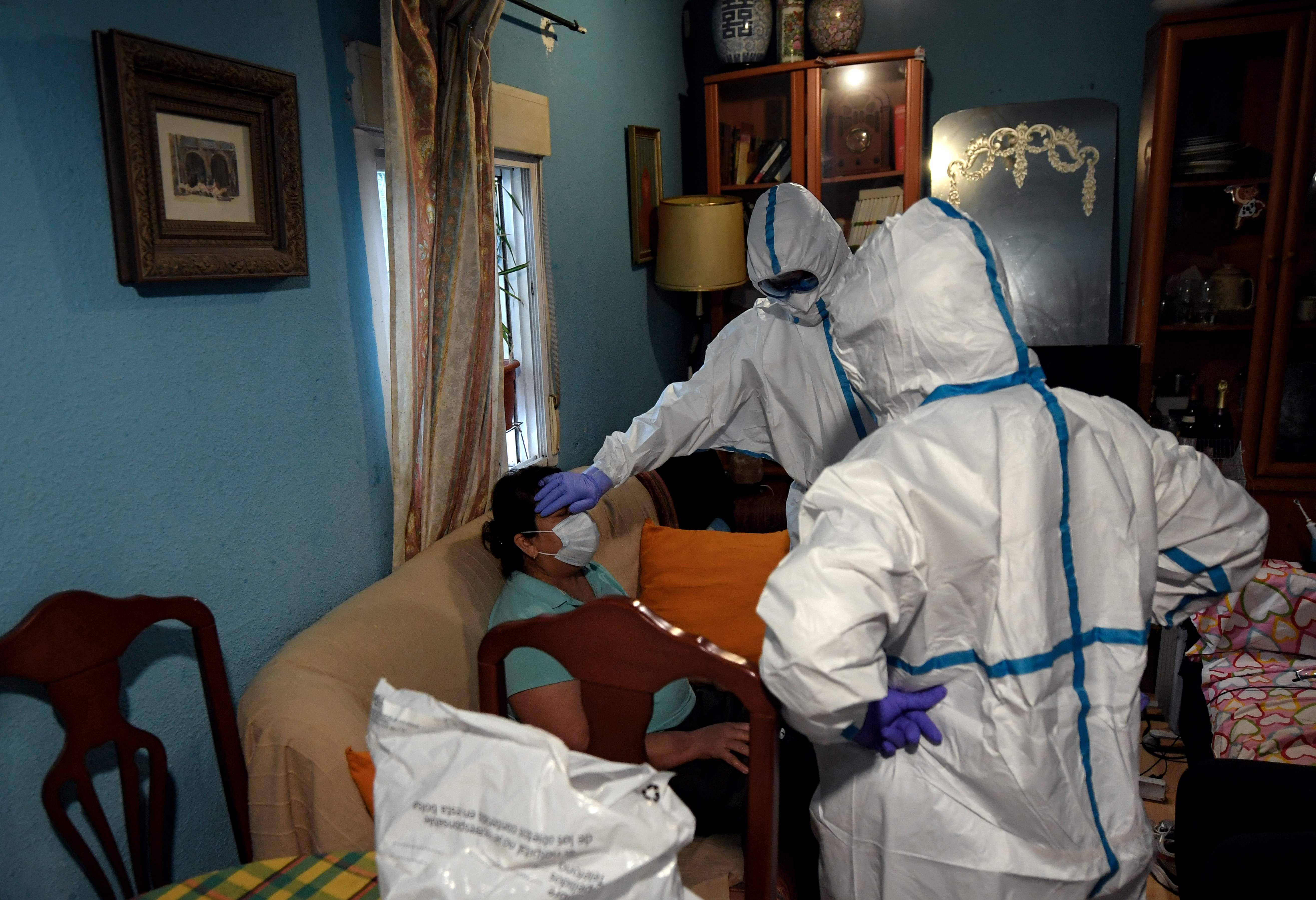 Petugas medis mengenakan APD memeriksa warga yang diduga mengidap covid-19 di kediamannya di Madrid, Spanyol.