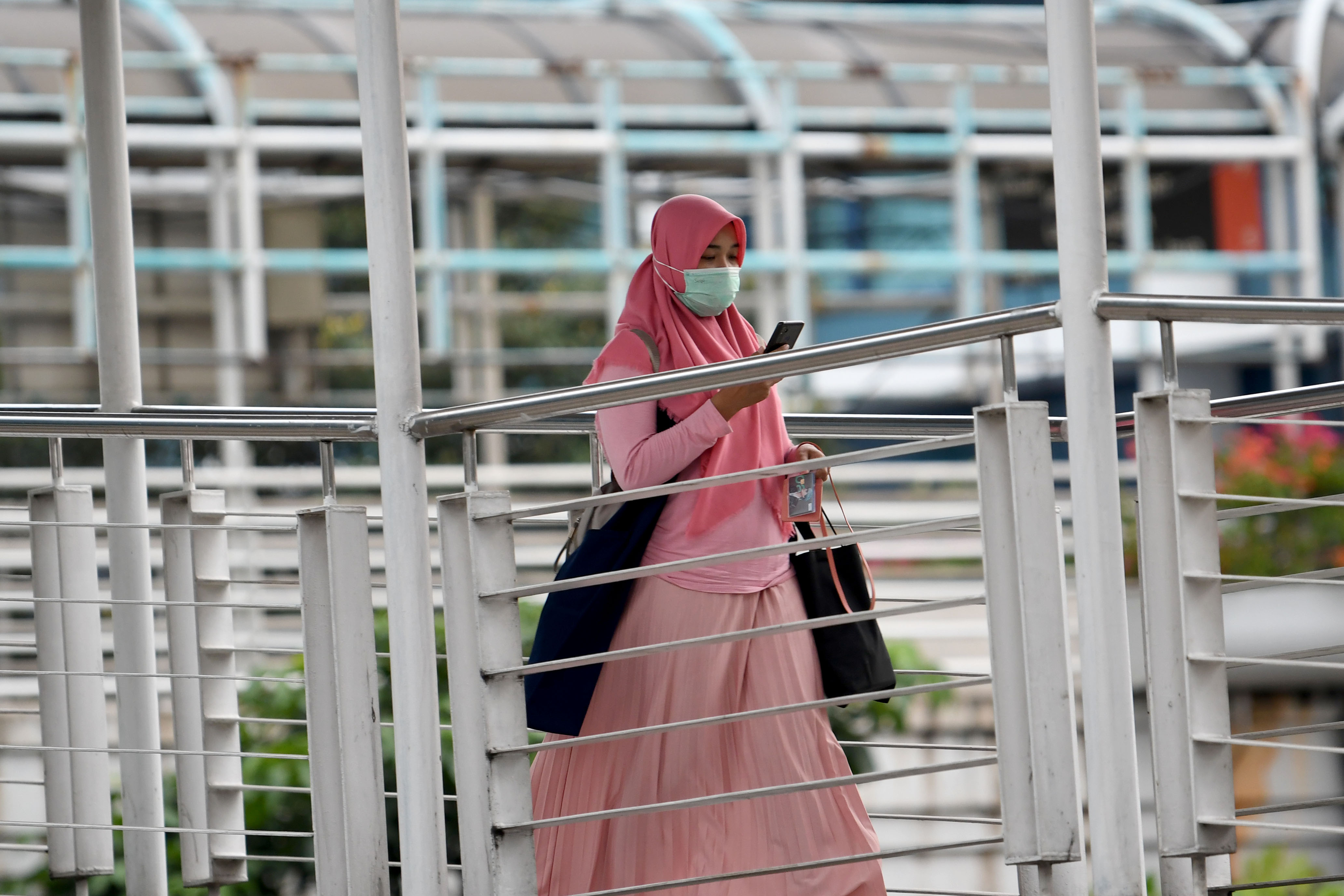 Seorang pejalan kaki mengenakan masker saat melintas di jembatan penyeberan orang menuju Halte Trans-Jakarta.