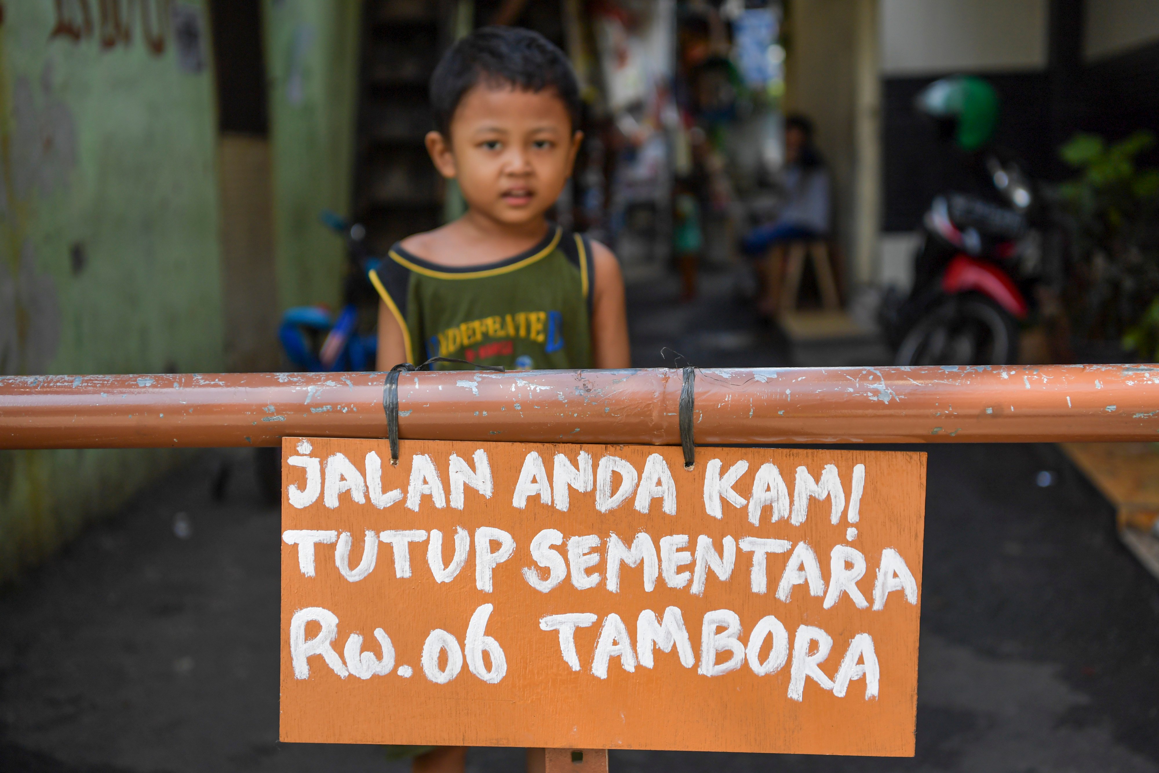 Seorang bocah berdiri di belakang portal karantina wilayah di kawasan Tambora, Jakarta, Jumat (3/4).