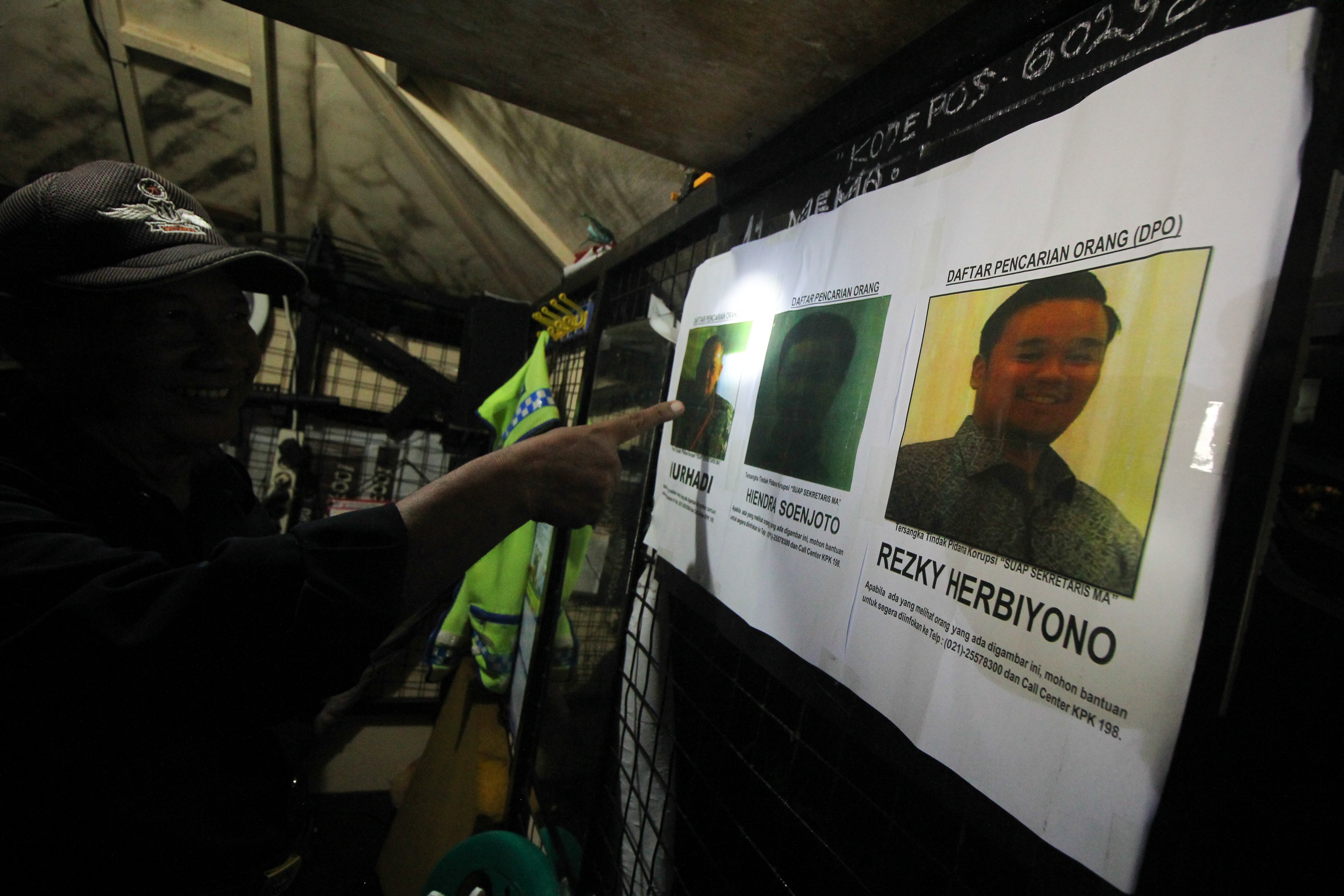 Petugas keamanan mengamati selebaran foto DPO yang ditempel petugas KPK yang mendatangi salah satu rumah di Perumahan Pandugo I, Surabaya