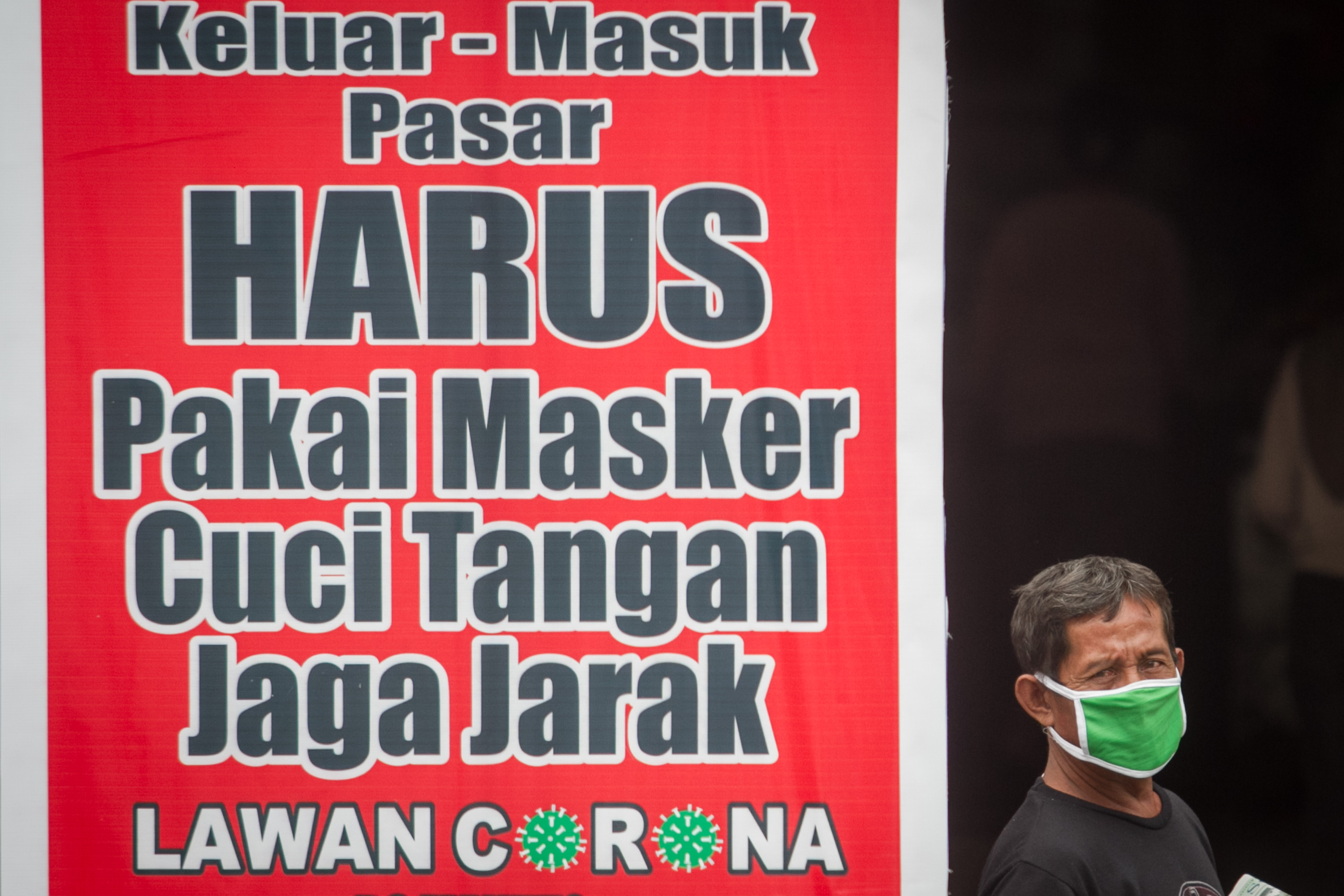  Warga melintas didekat papan himbauan wajib mengenakan masker, cuci tangan dan jaga jarak di Pasar Gede, Solo, Jawa Tengah.