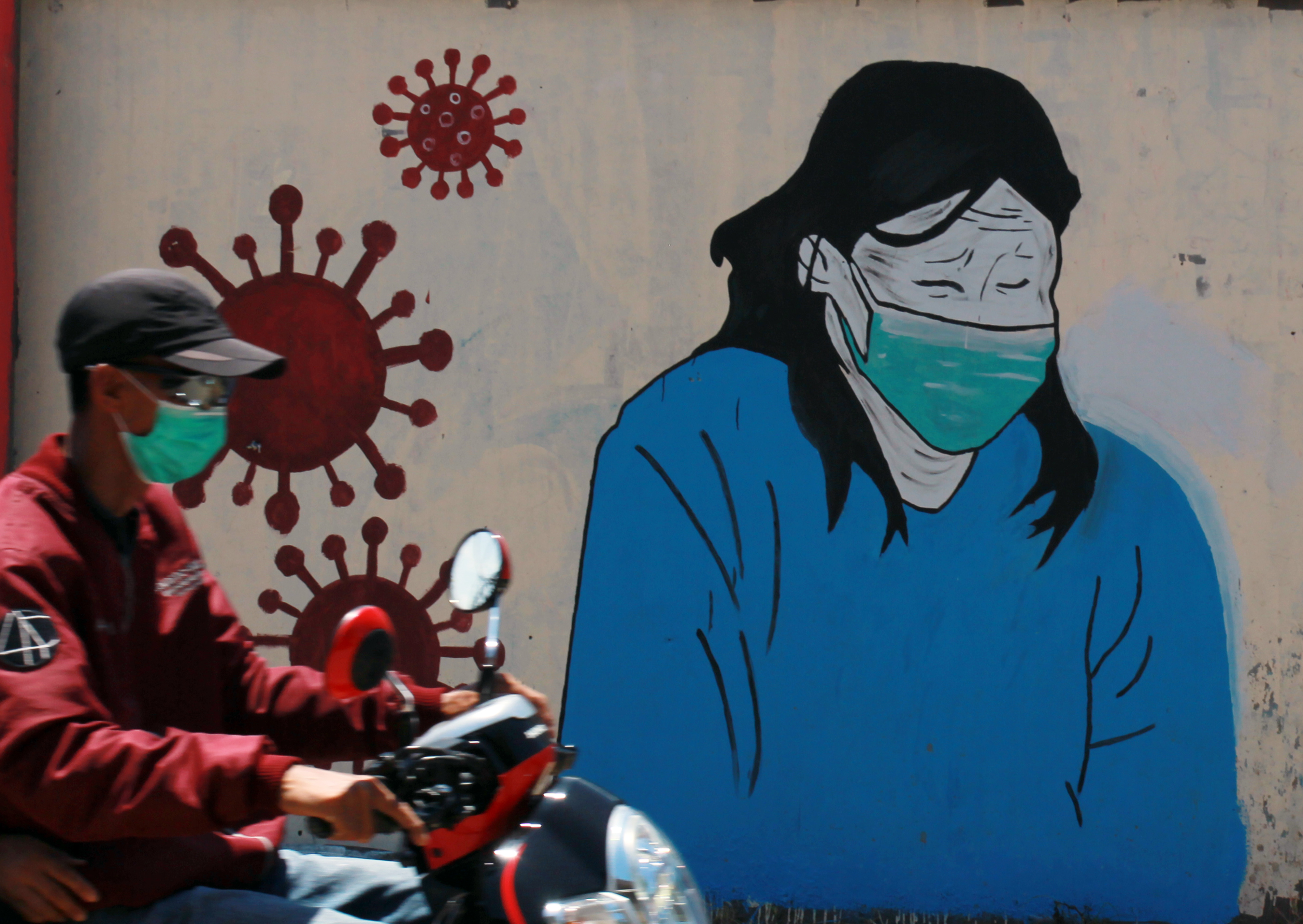 Pengendara motor melintasi mural tentang pandemi covid-19 di wilayah Tangerang, Banten.