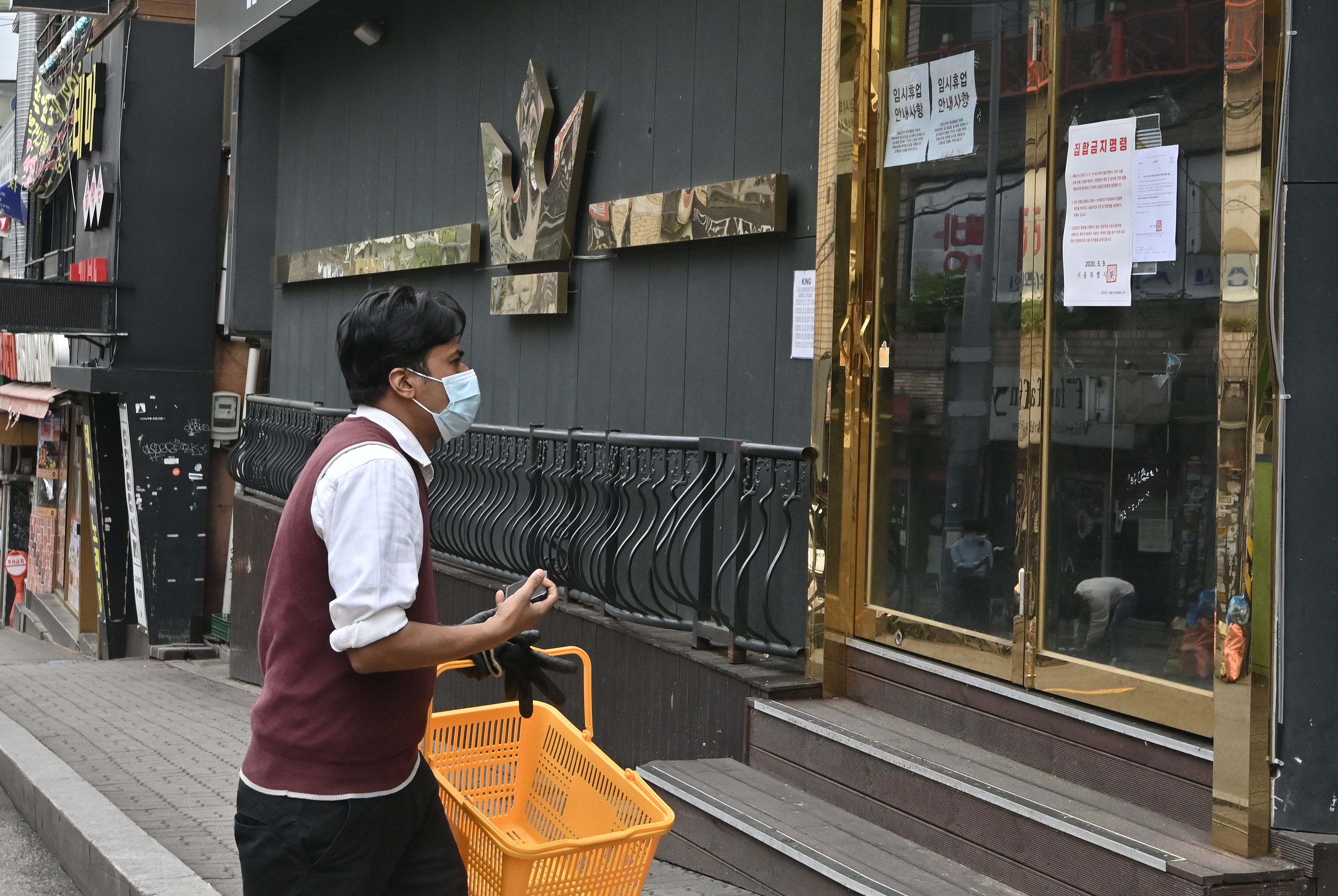 Seorang pria memakai masker berjalan melewati klub malam yang kini ditutup setelah kunjungan pasien covid-19 (10/5)