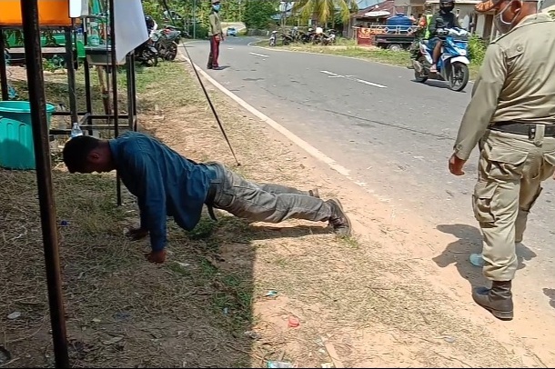 Seorang pemuda dihukum push up karena tidak mengenakan masker. 
